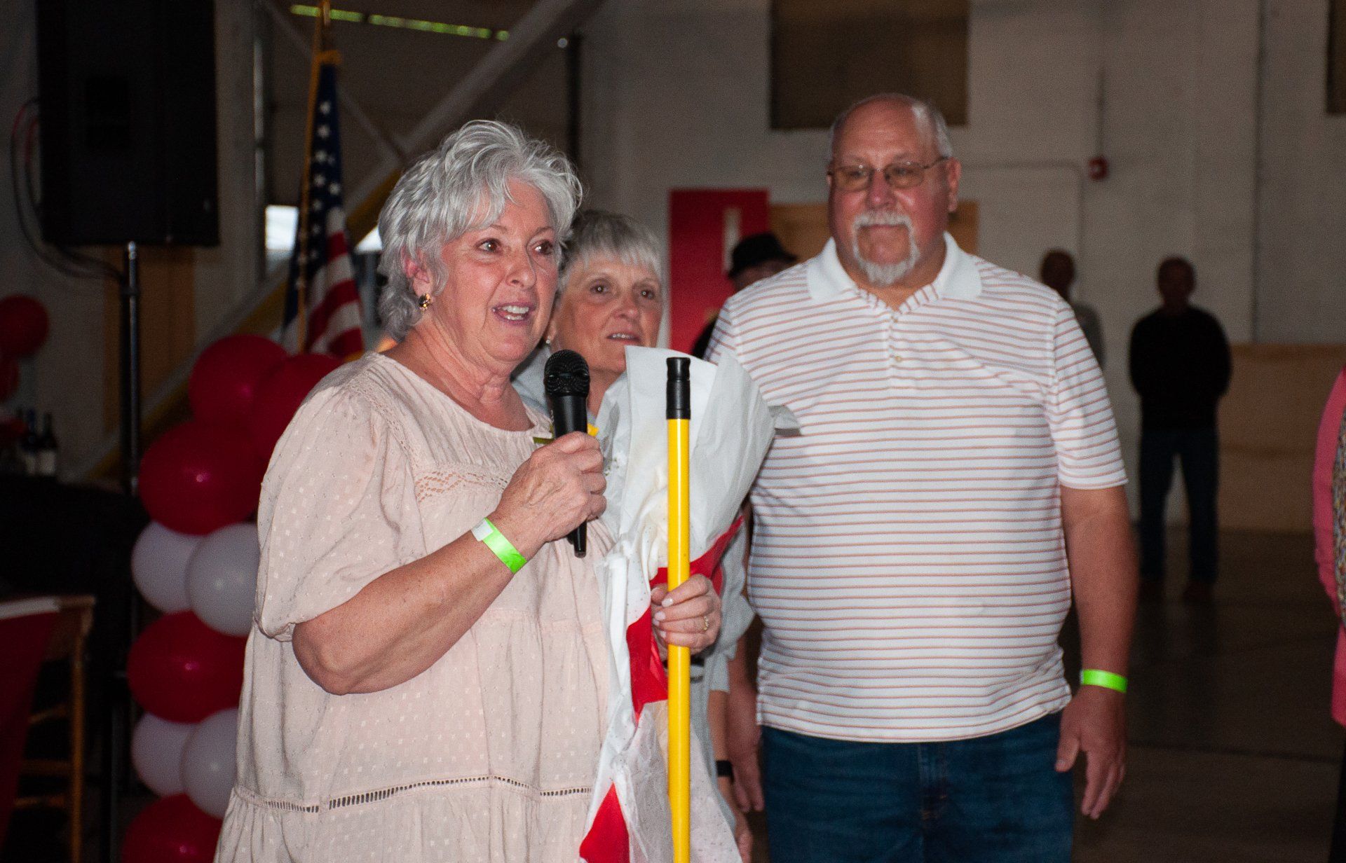 Two people standing indoors at an event, smiling and holding a microphone and a striped pole.