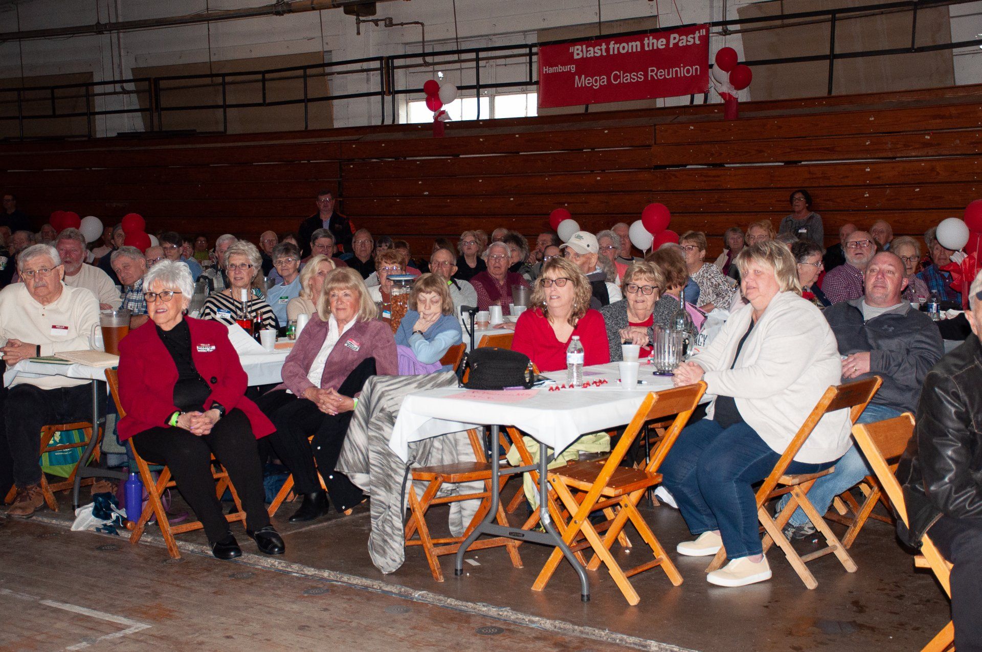 Audience seated at tables in a gymnasium watching an indoor event