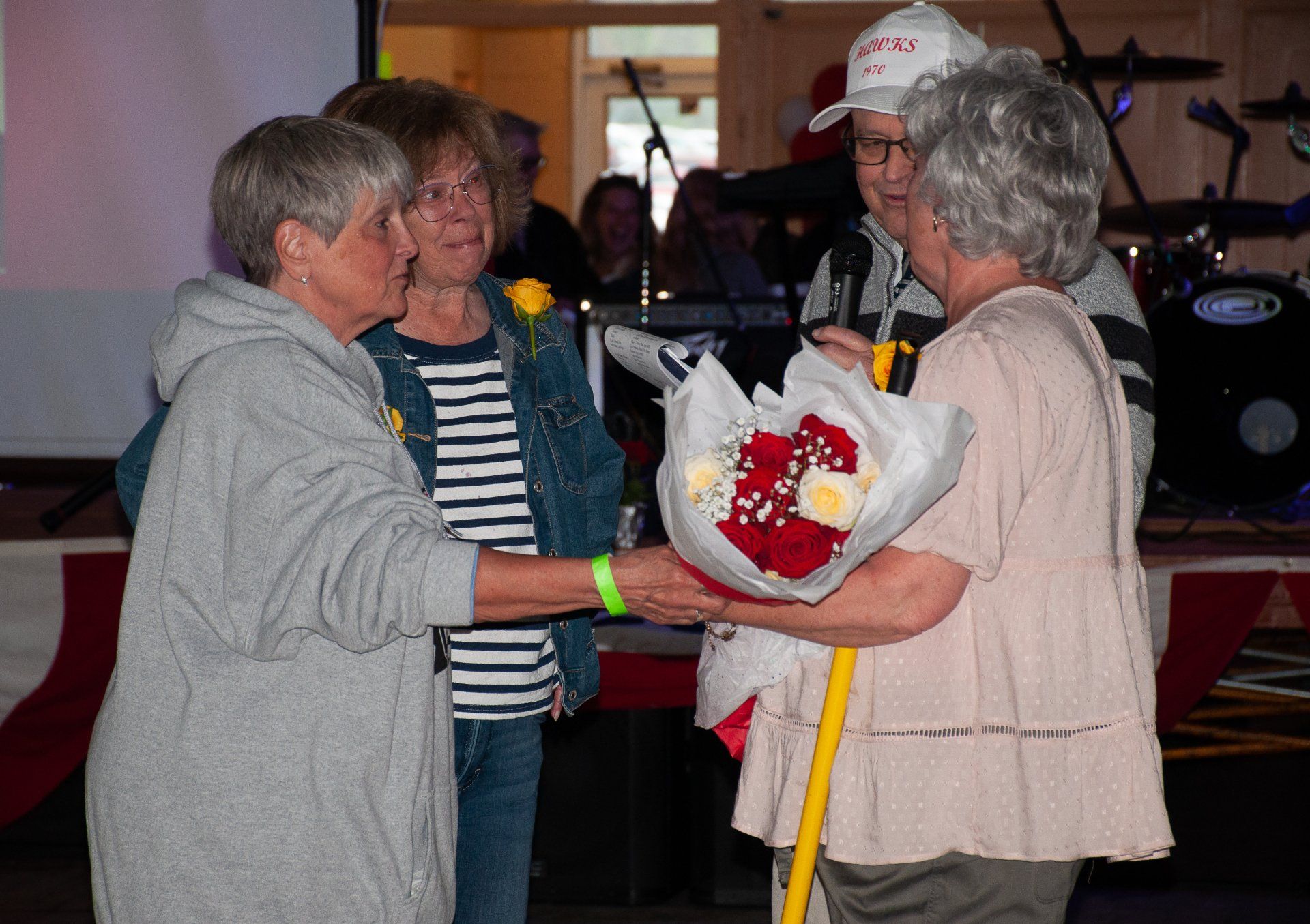 Two people exchange a bouquet at an indoor event with musical instruments in the background