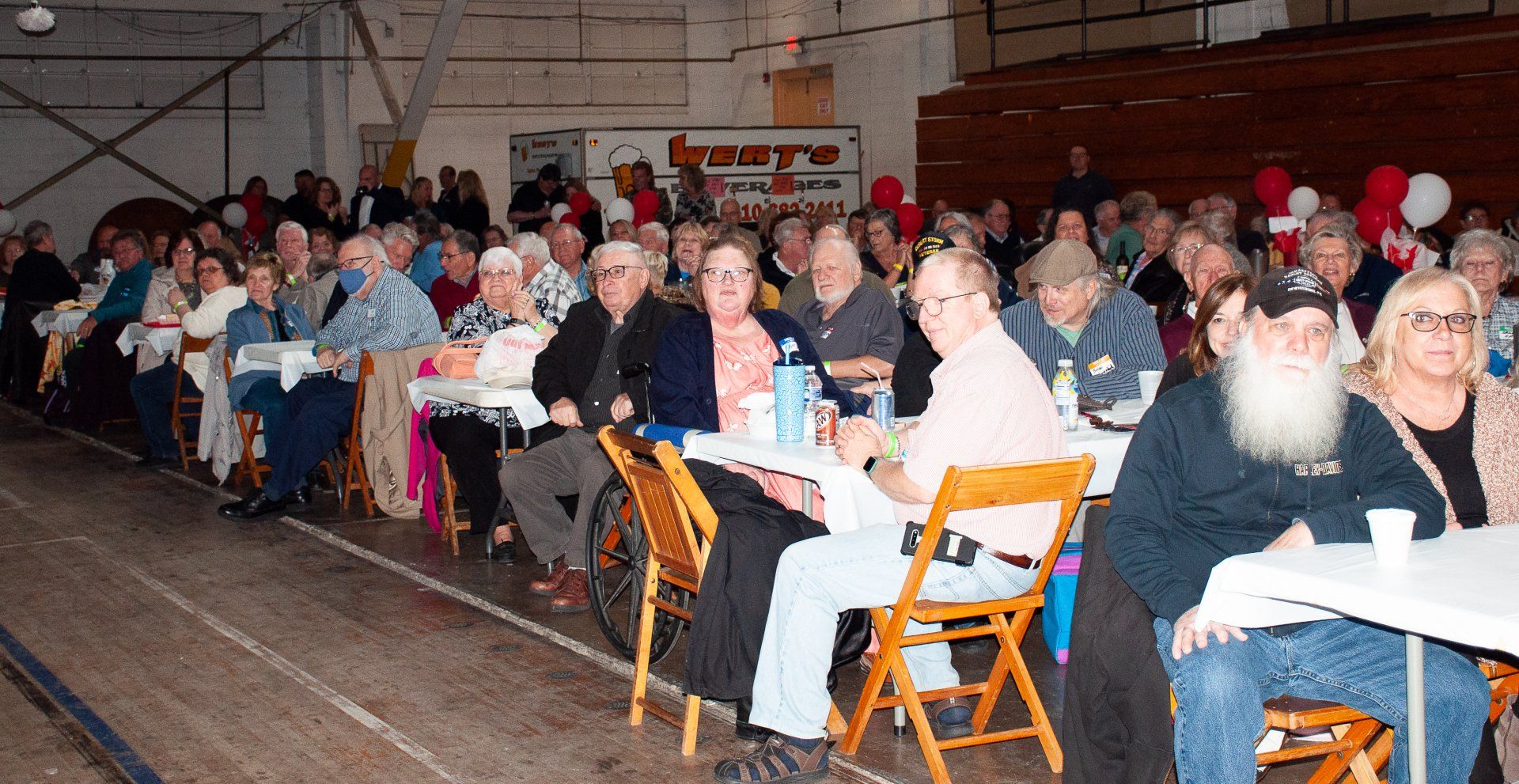 Large group seated at long tables in a warehouse, listening or socializing during an indoor gathering