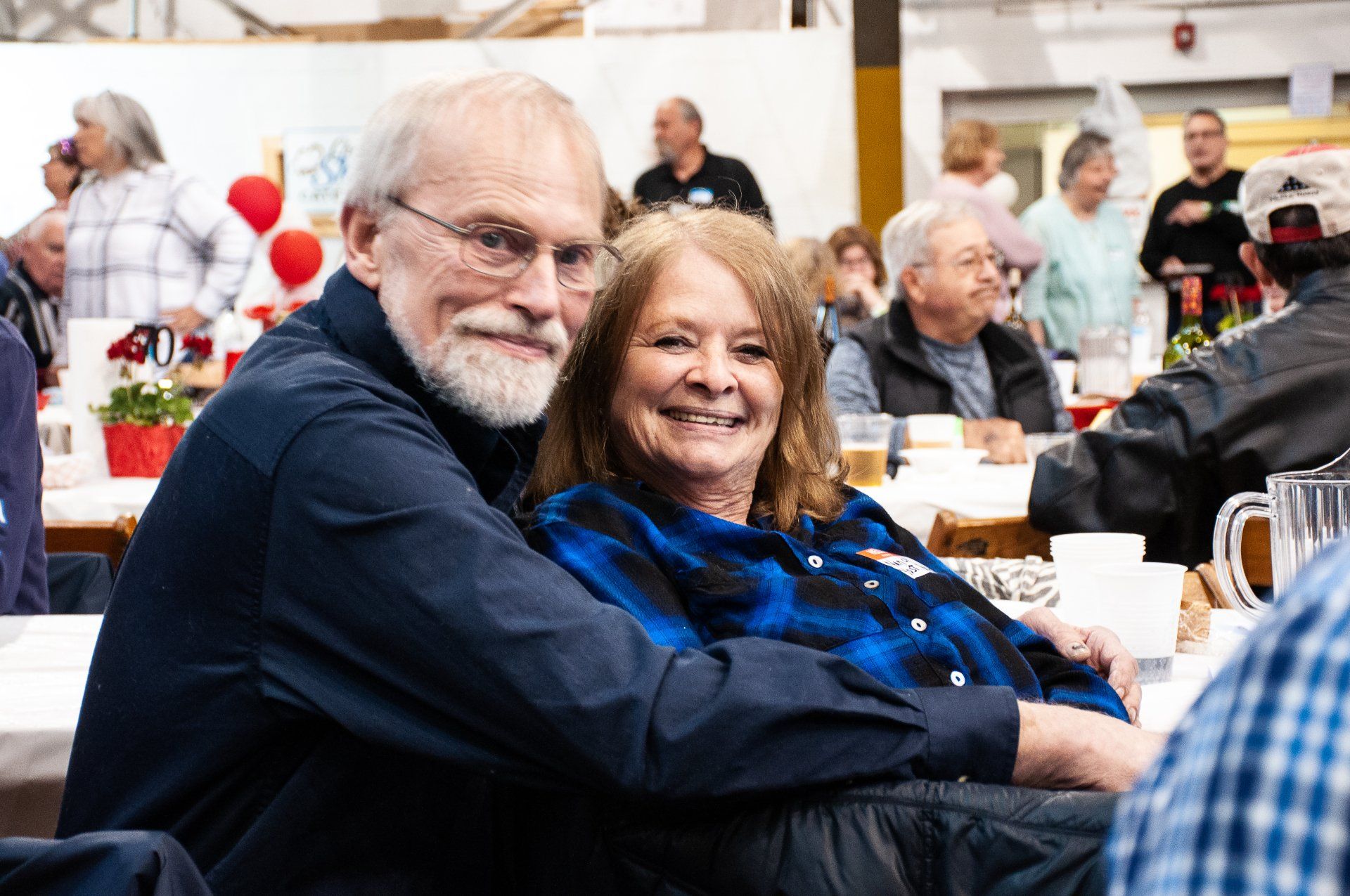 Smiling couple seated at a banquet table, looking at the camera in a busy indoor gathering
