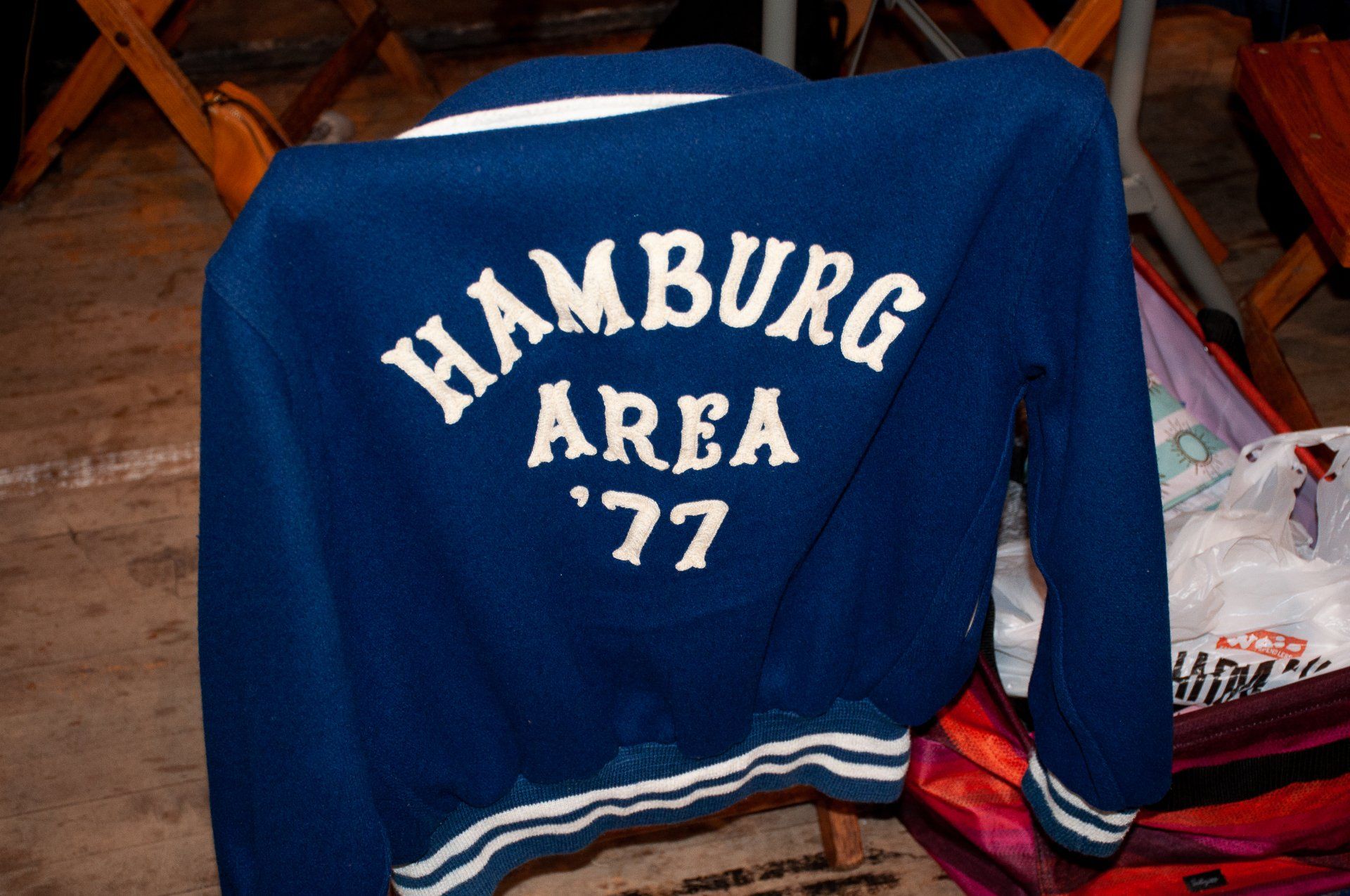 Blue “Hamburg Area ’77” jacket draped over a chair with red-striped sleeves visible