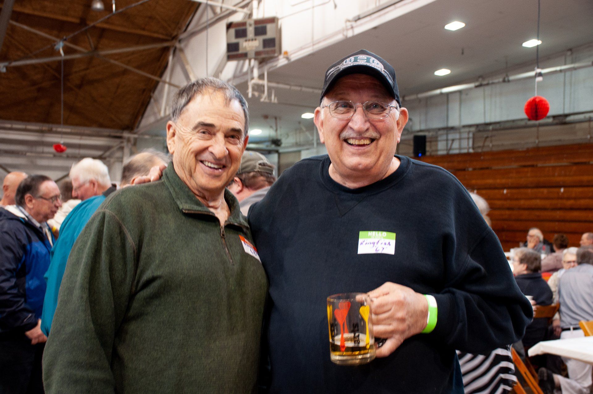 Two men smiling and posing indoors at a social gathering, one holding a drink.