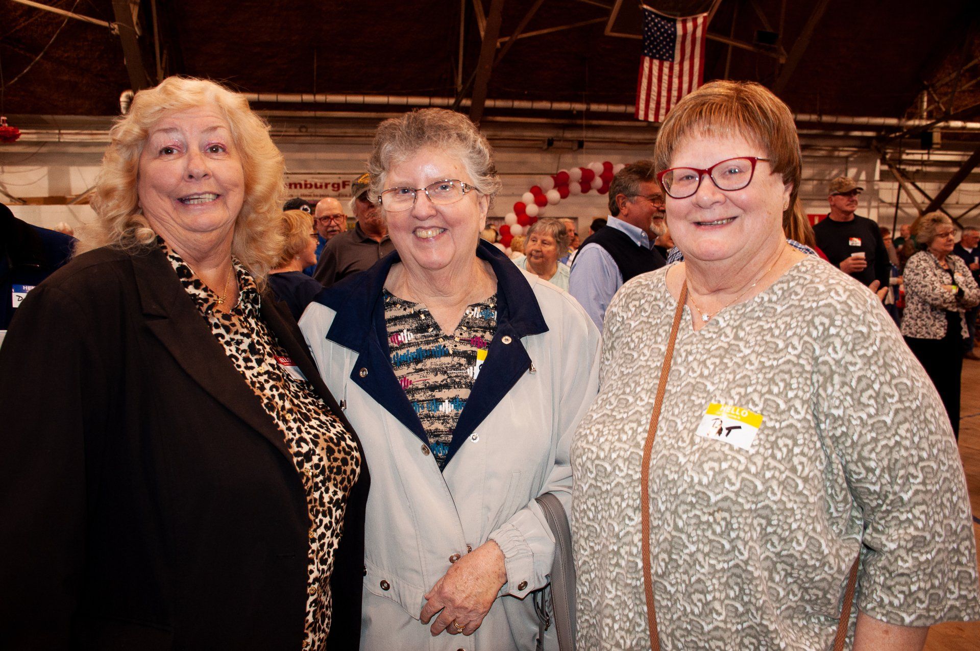 Three women smiling at an indoor event, standing together in front of a carousel backdrop