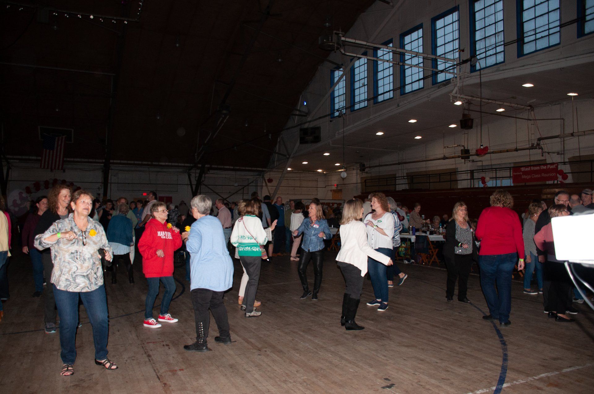 People dancing in a gymnasium with high windows and wooden floors