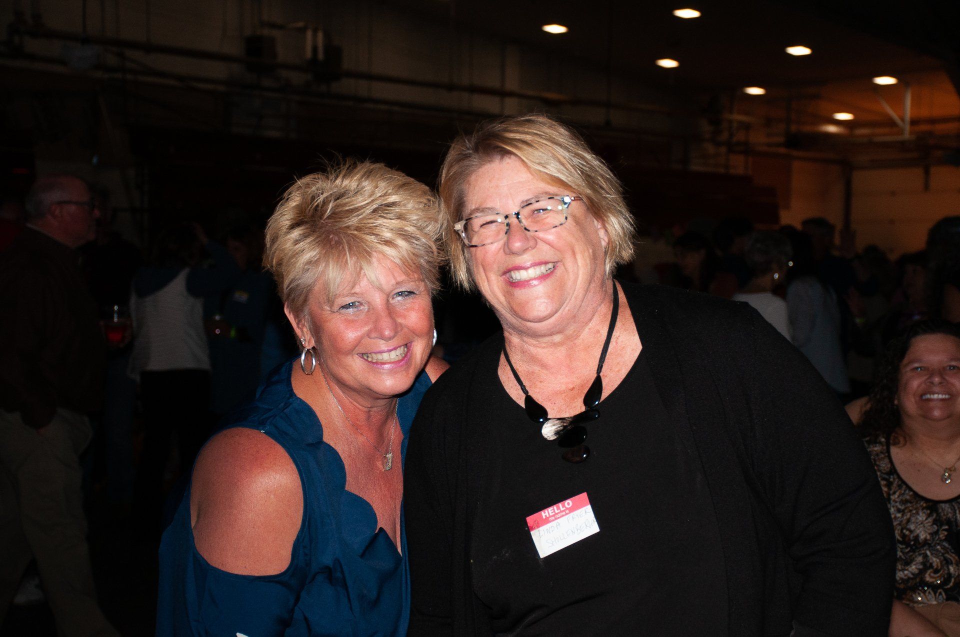 Two smiling people posing together at a dimly lit indoor event