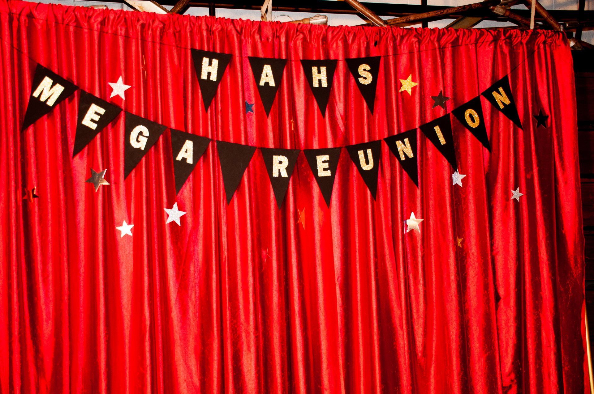 Red curtain backdrop with black pennant banners spelling “Maks Mega Reunion” and small white stars