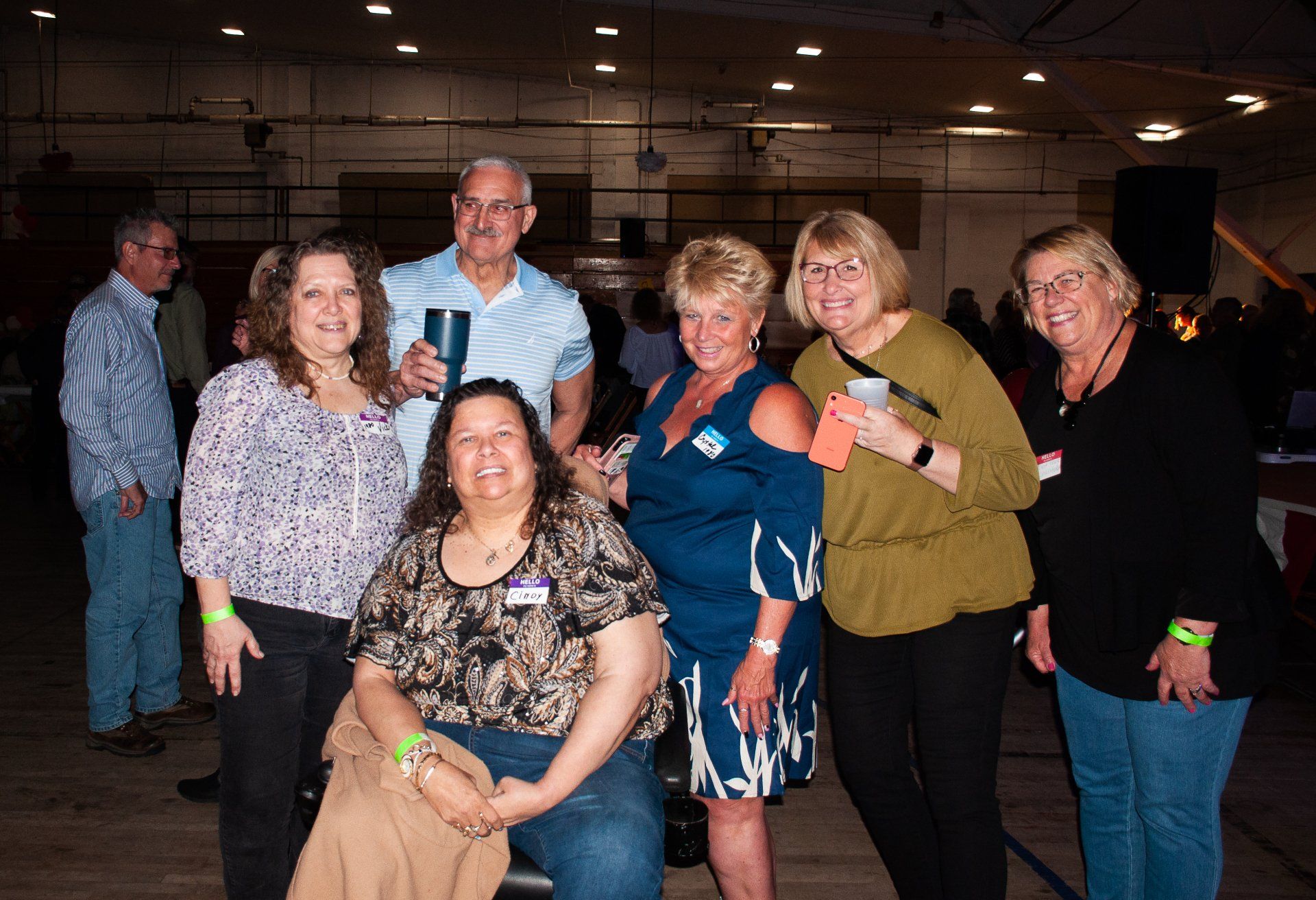 Group of six people smiling indoors at a social event, with one seated in front and others standing behind.
