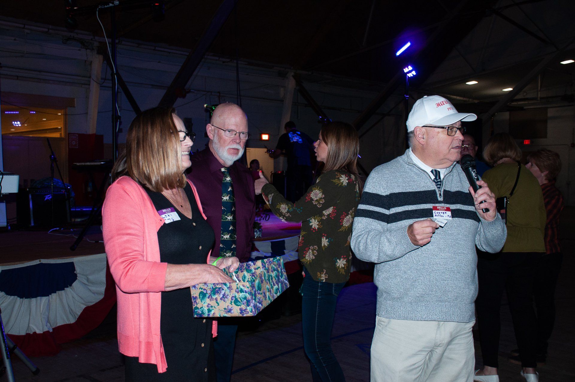 Three people chatting at a dim indoor event, one holding a gift bag and another holding a drink.
