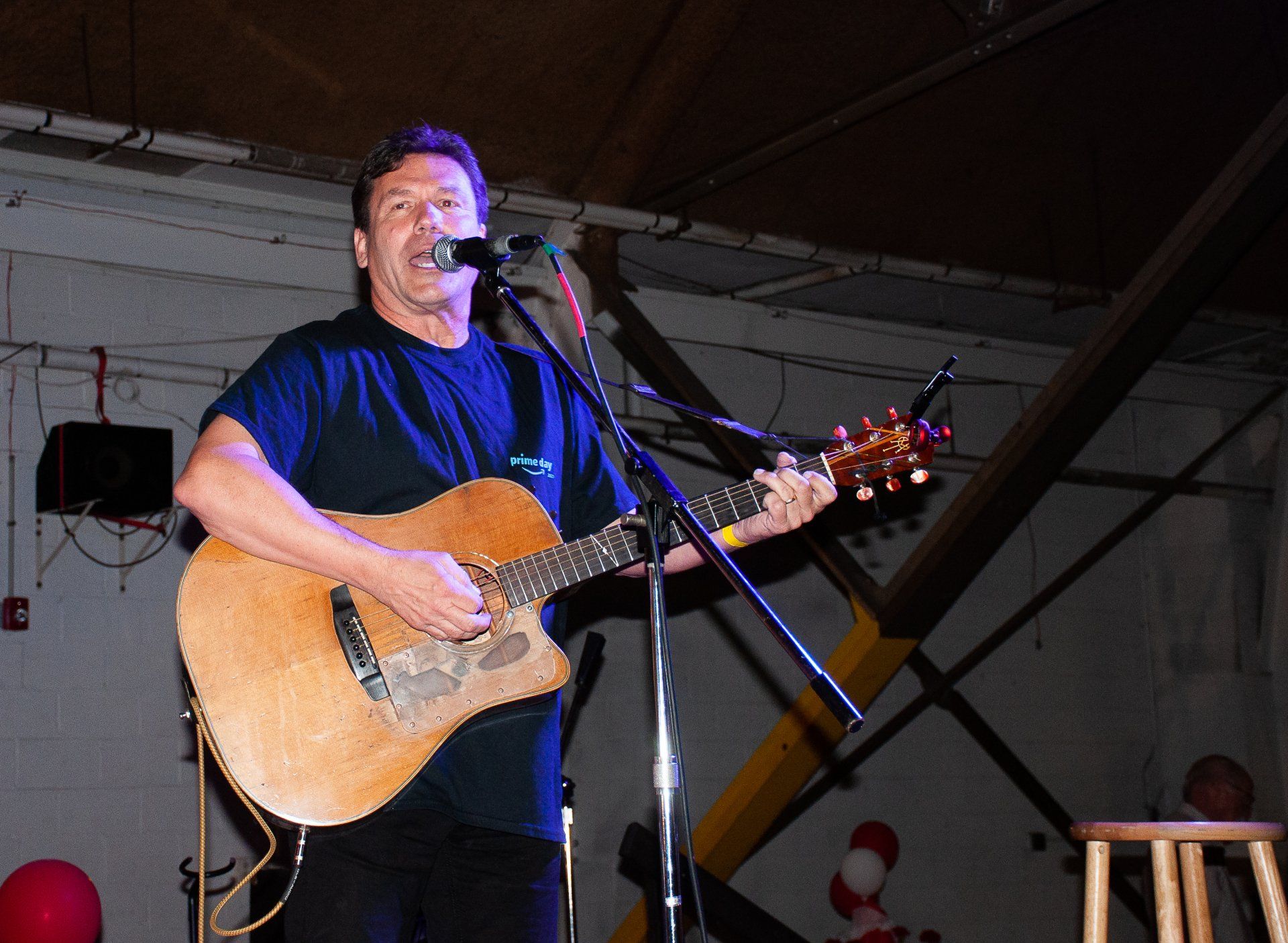 Singer playing acoustic guitar on stage, singing into a microphone under blue and purple lights