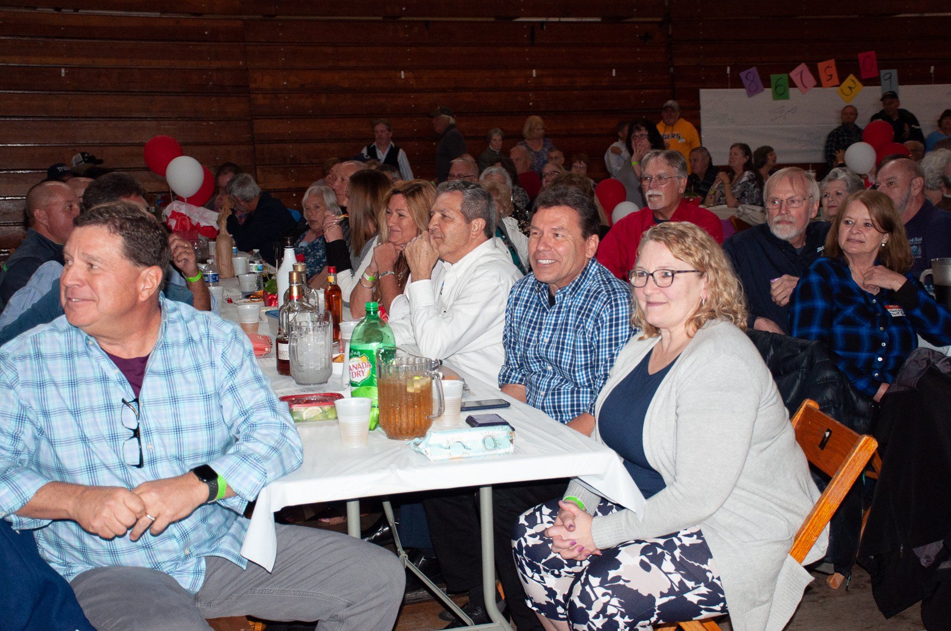 Audience seated at tables in a hall, listening and chatting during an indoor event