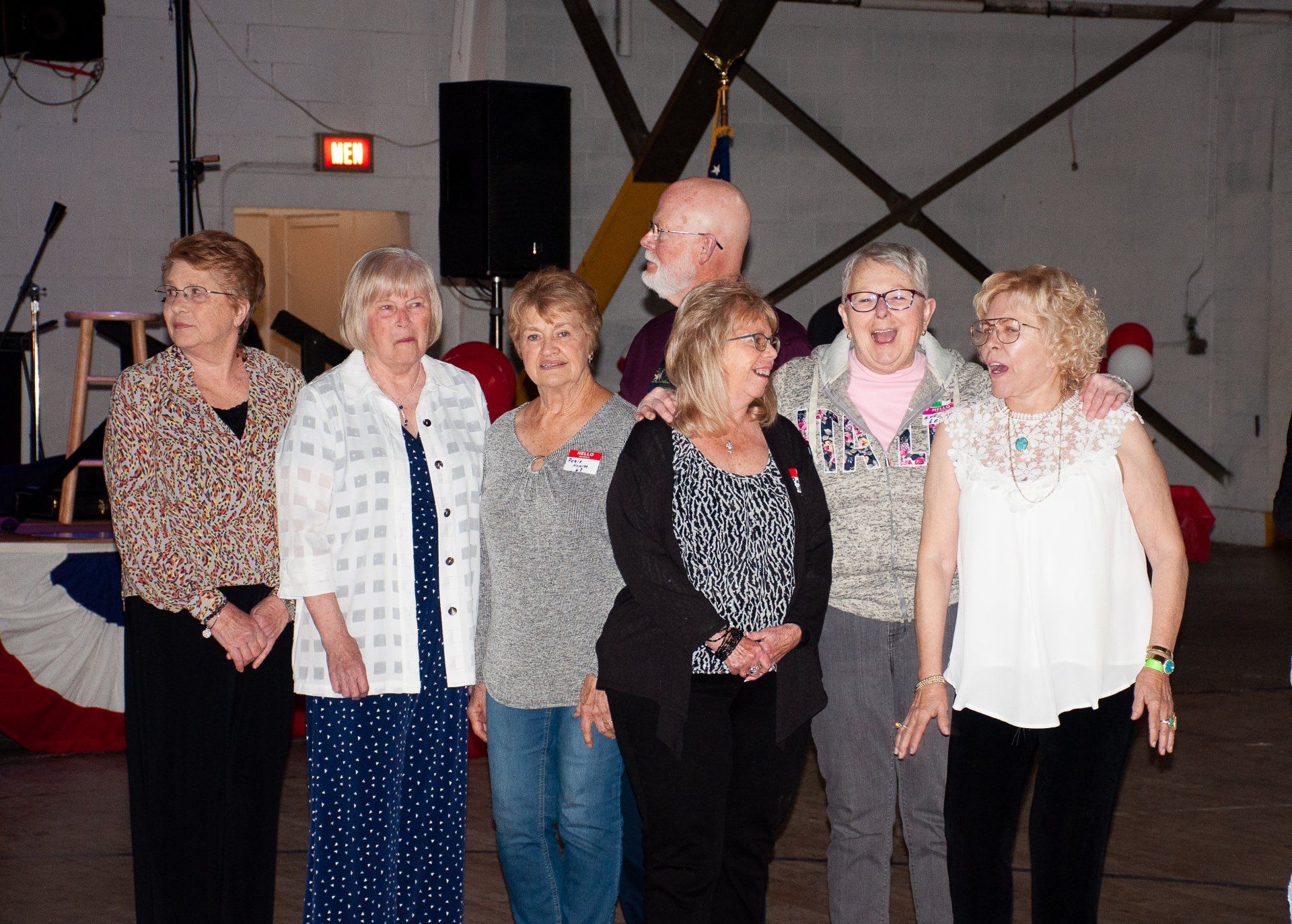 Six people standing together indoors on a stage, smiling and posing for a group photo.
