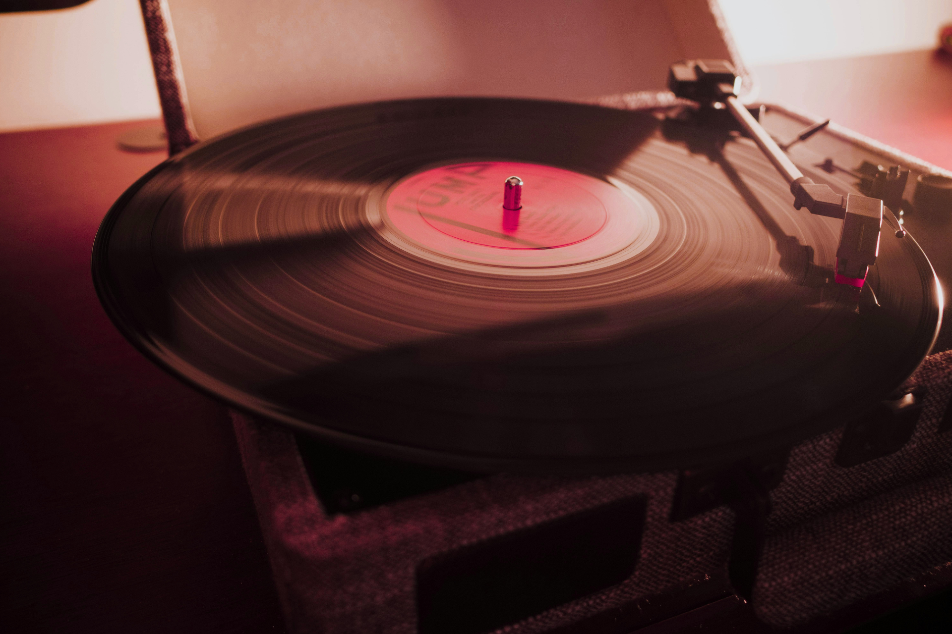 Vinyl record spinning on a turntable with a pink center label under warm light