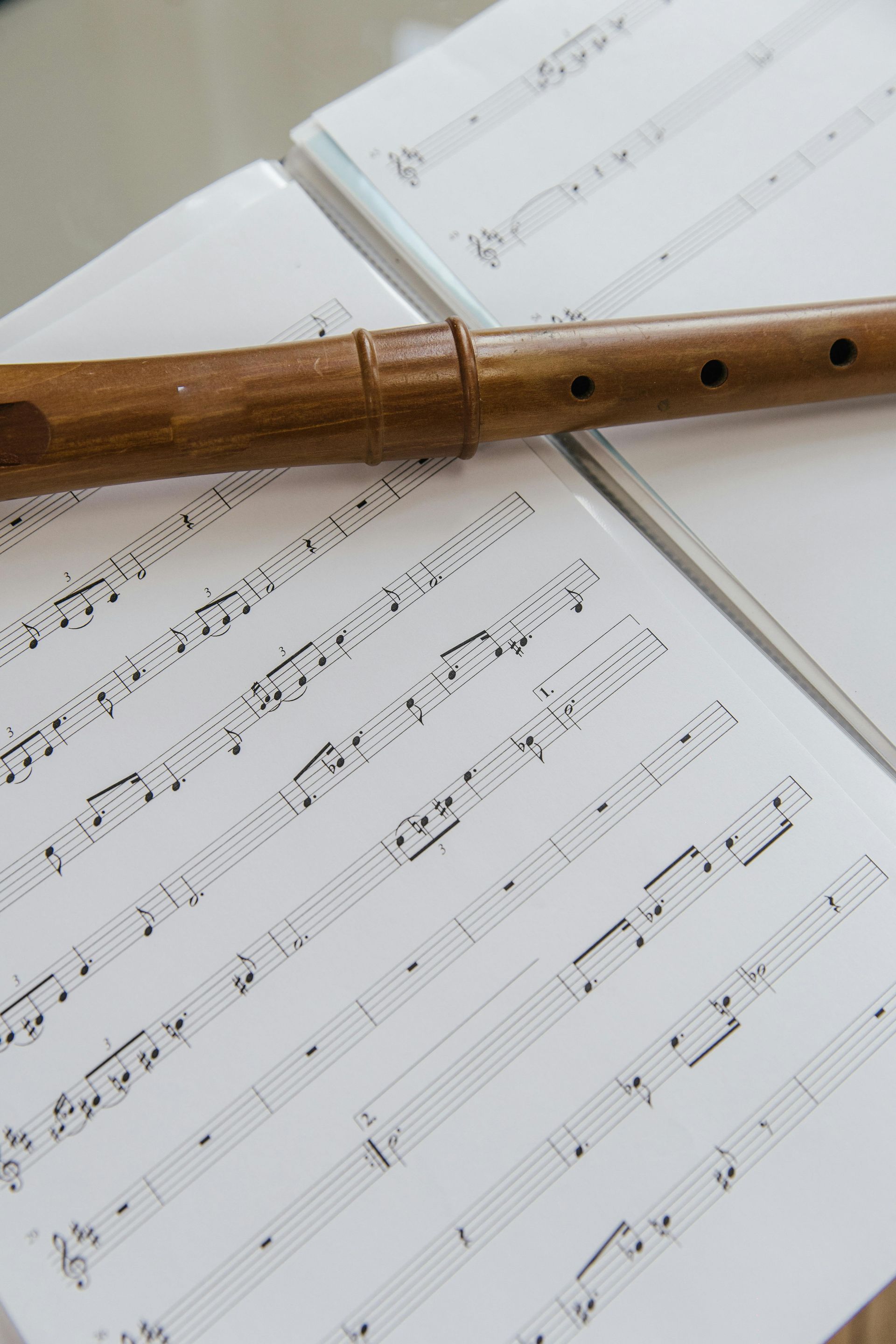 Wooden flute resting diagonally over sheet music on a white surface.
