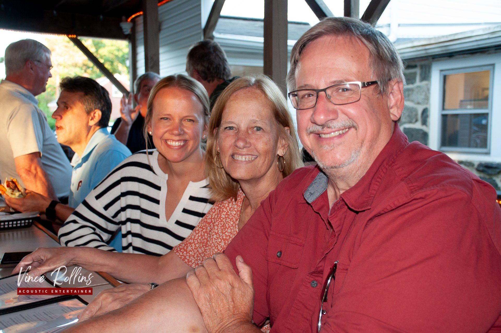 Three smiling people seated at a table on a boat, with warm sunset light on the water.