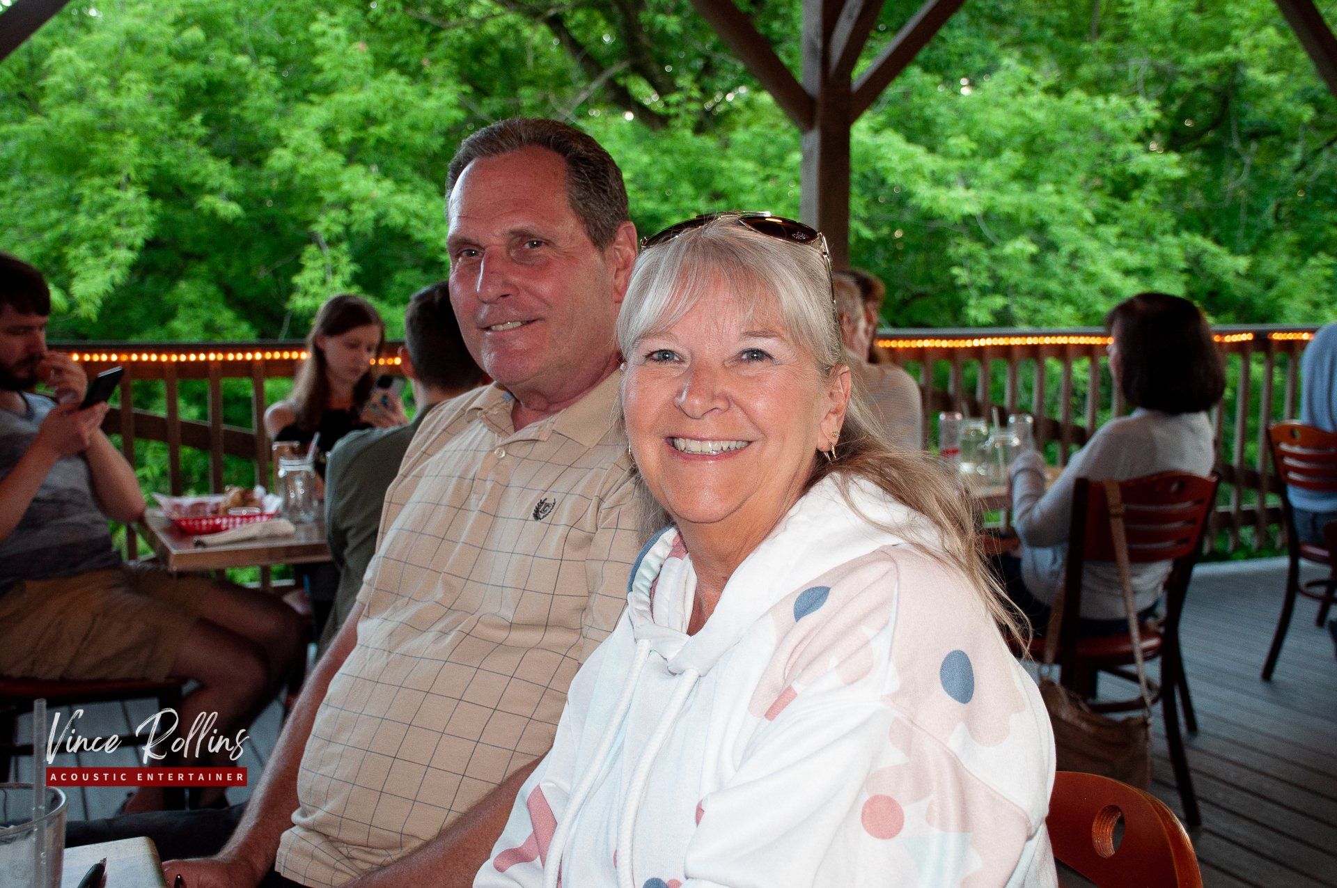 Smiling couple seated at an outdoor patio table with green trees in the background
