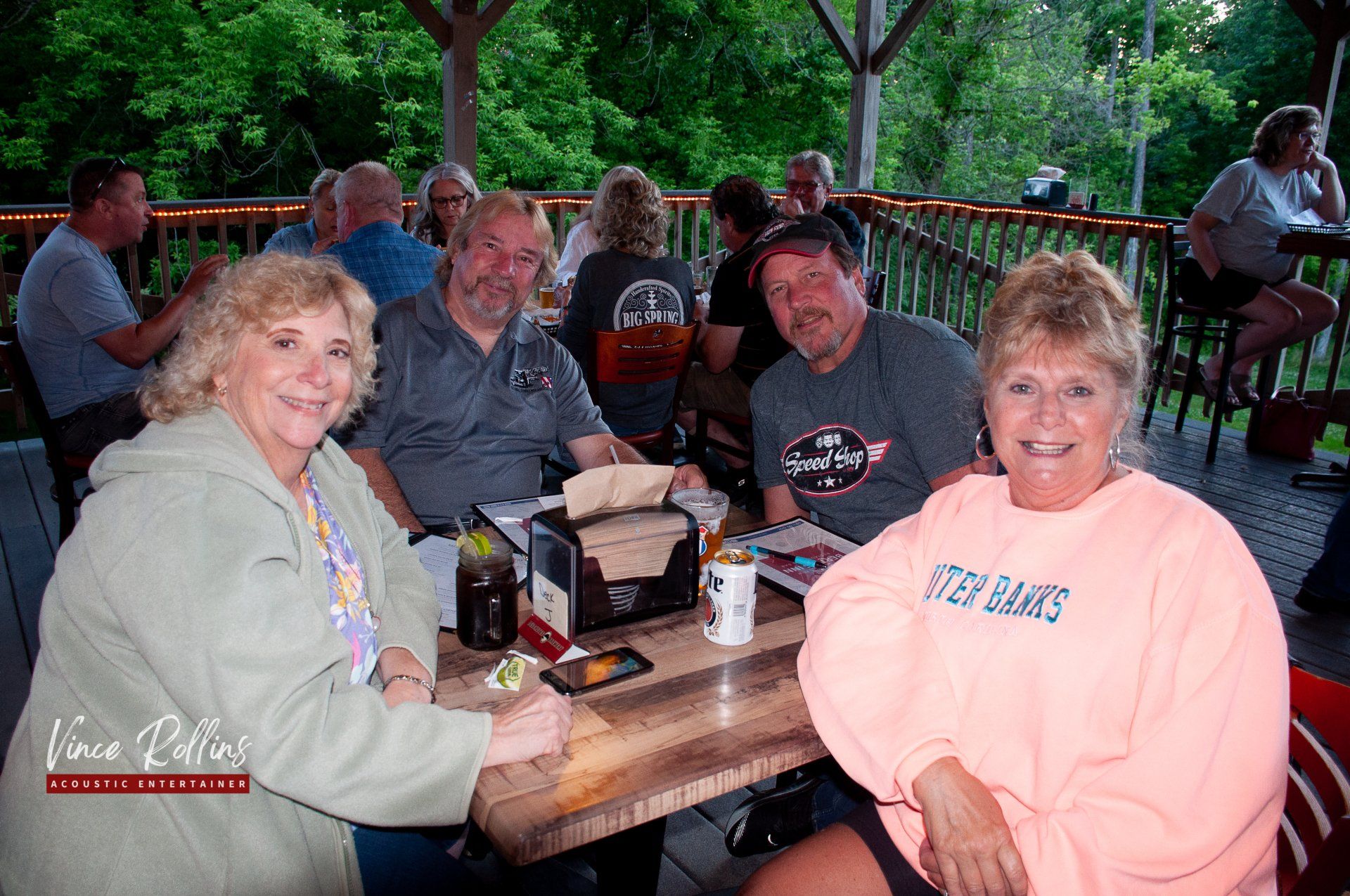 People seated at a picnic table under a covered outdoor pavilion, smiling and socializing.