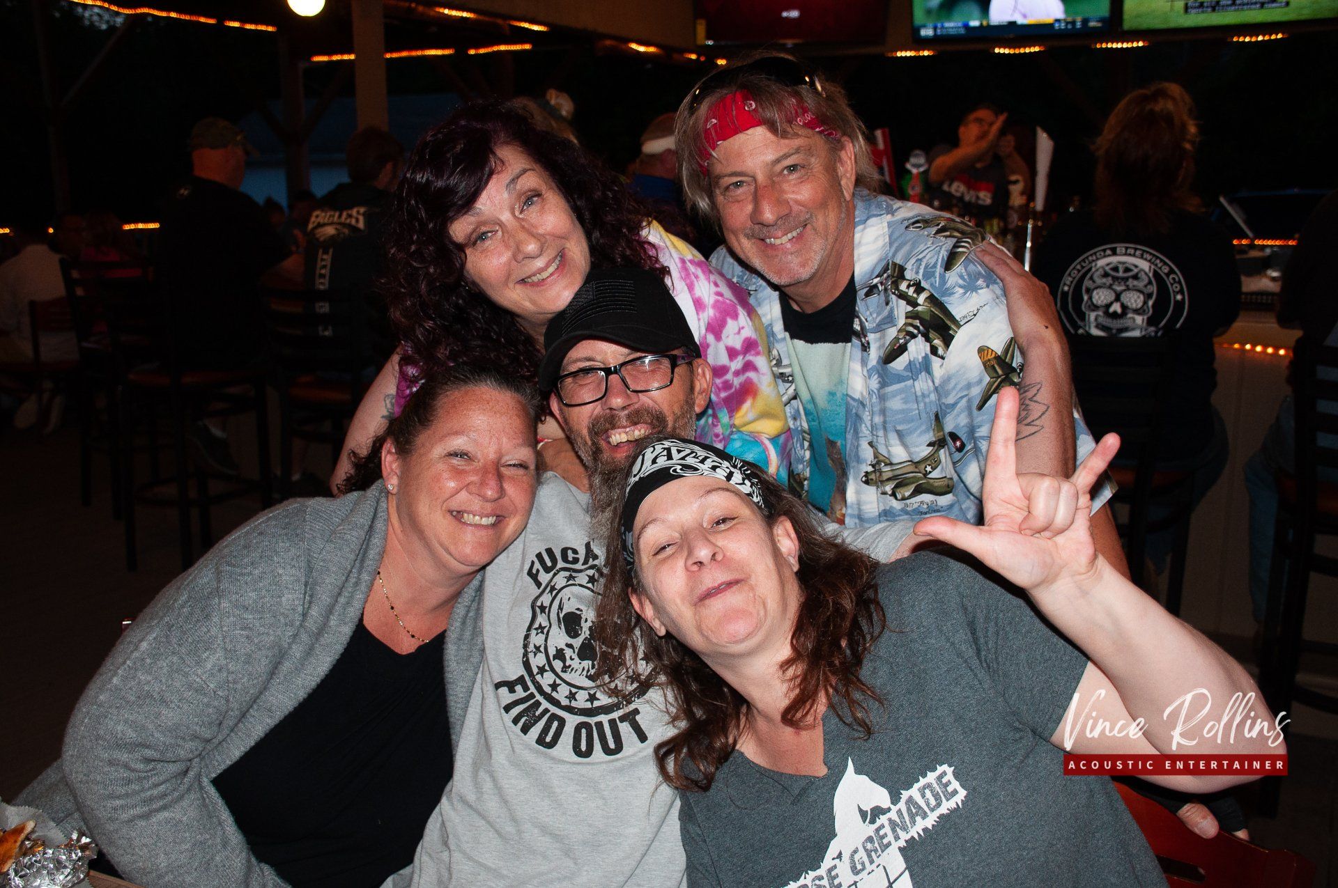 Five friends smiling and posing together in a dimly lit bar or nightclub