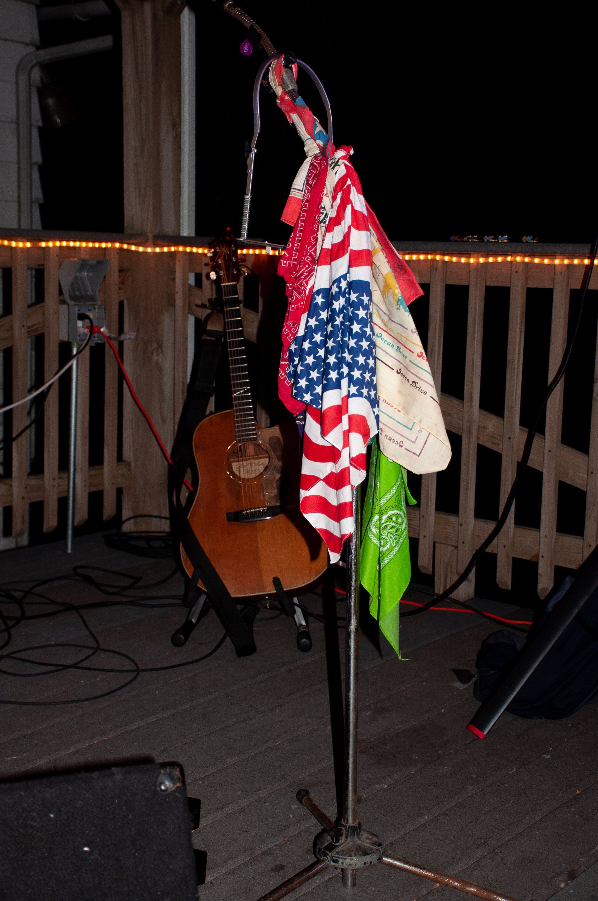 American flag-patterned cloths hanging on a microphone stand on a dimly lit outdoor deck near a guitar