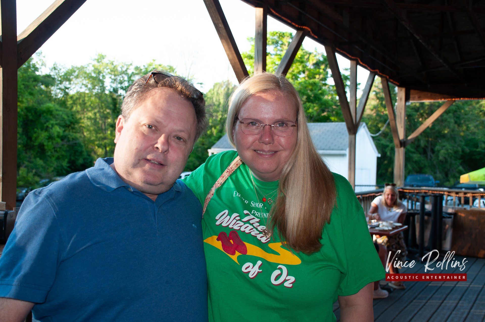 Two people posing together under a wooden pavilion at an outdoor gathering
