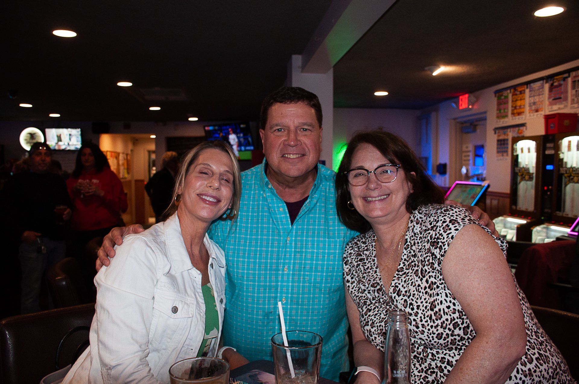 Three people smiling at a table in a dimly lit bar or restaurant