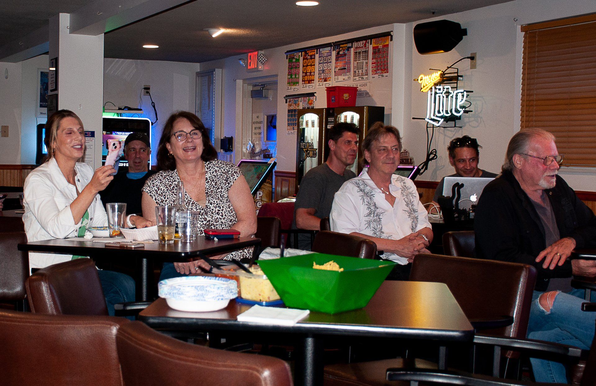 People seated at a bar in a cozy restaurant, chatting and drinking with a green bowl on a table.