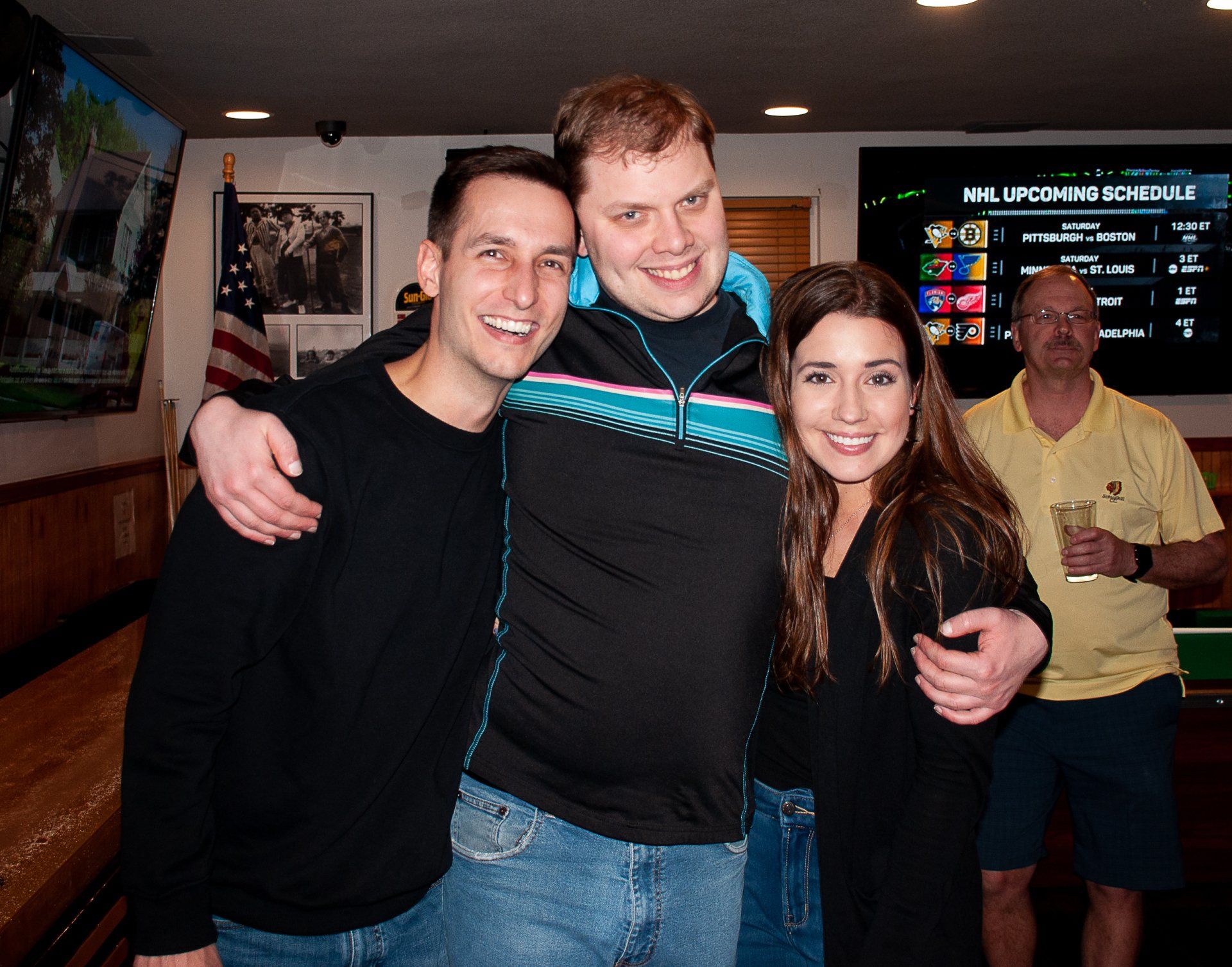 Three smiling people posing together indoors, with arcade machines in the background.