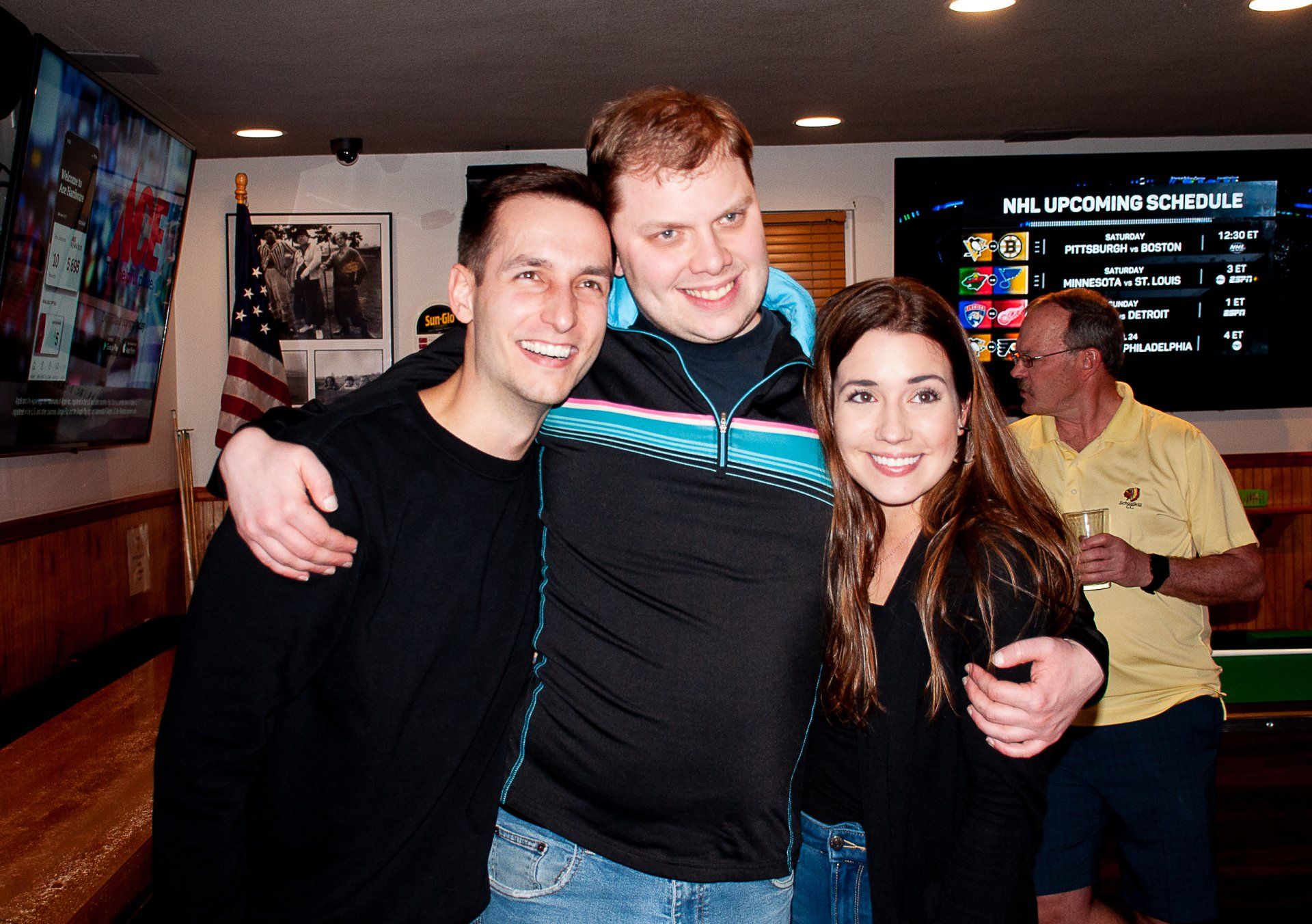 Three people smiling and posing together in a dimly lit indoor venue