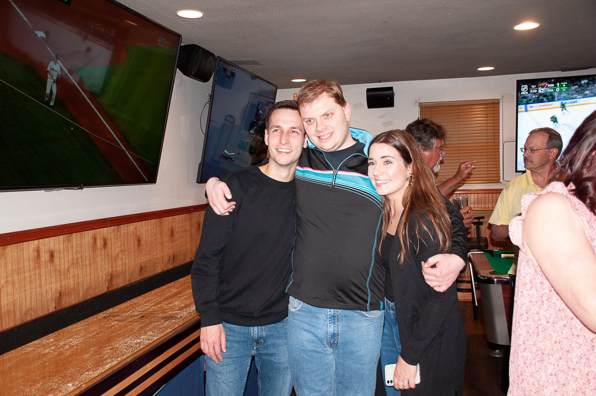 Three friends posing together in a bar, smiling with arms around each other