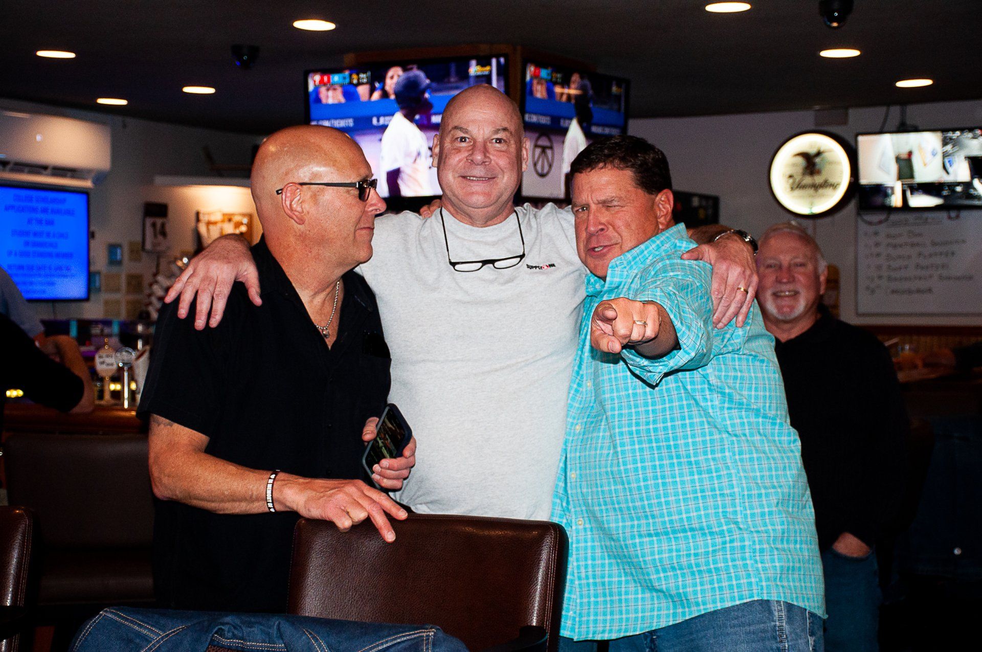 Four people smiling and posing together in a dimly lit bar, one pointing at the camera.