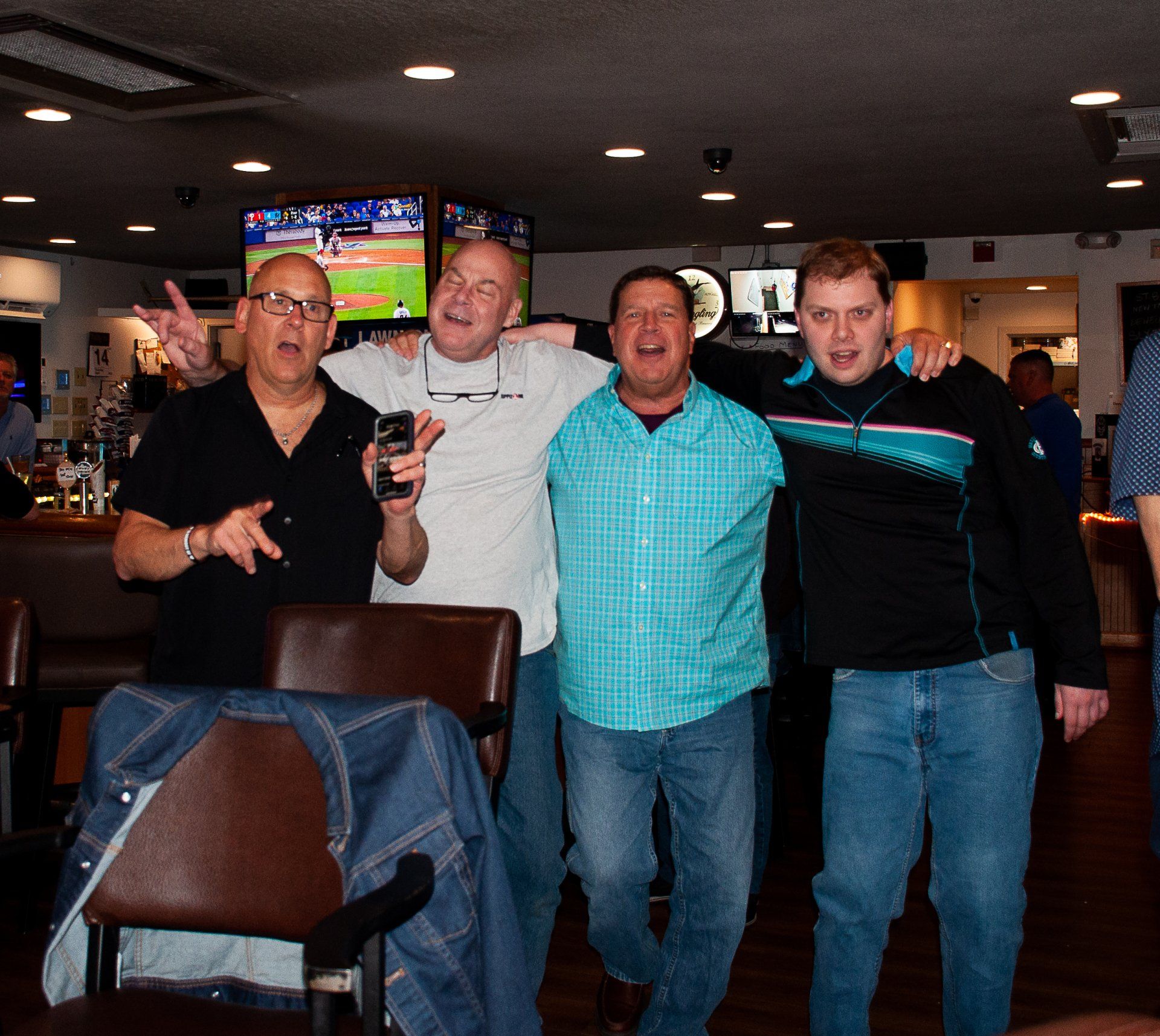 Four men posing together in a dim bar, smiling with drinks in hand.