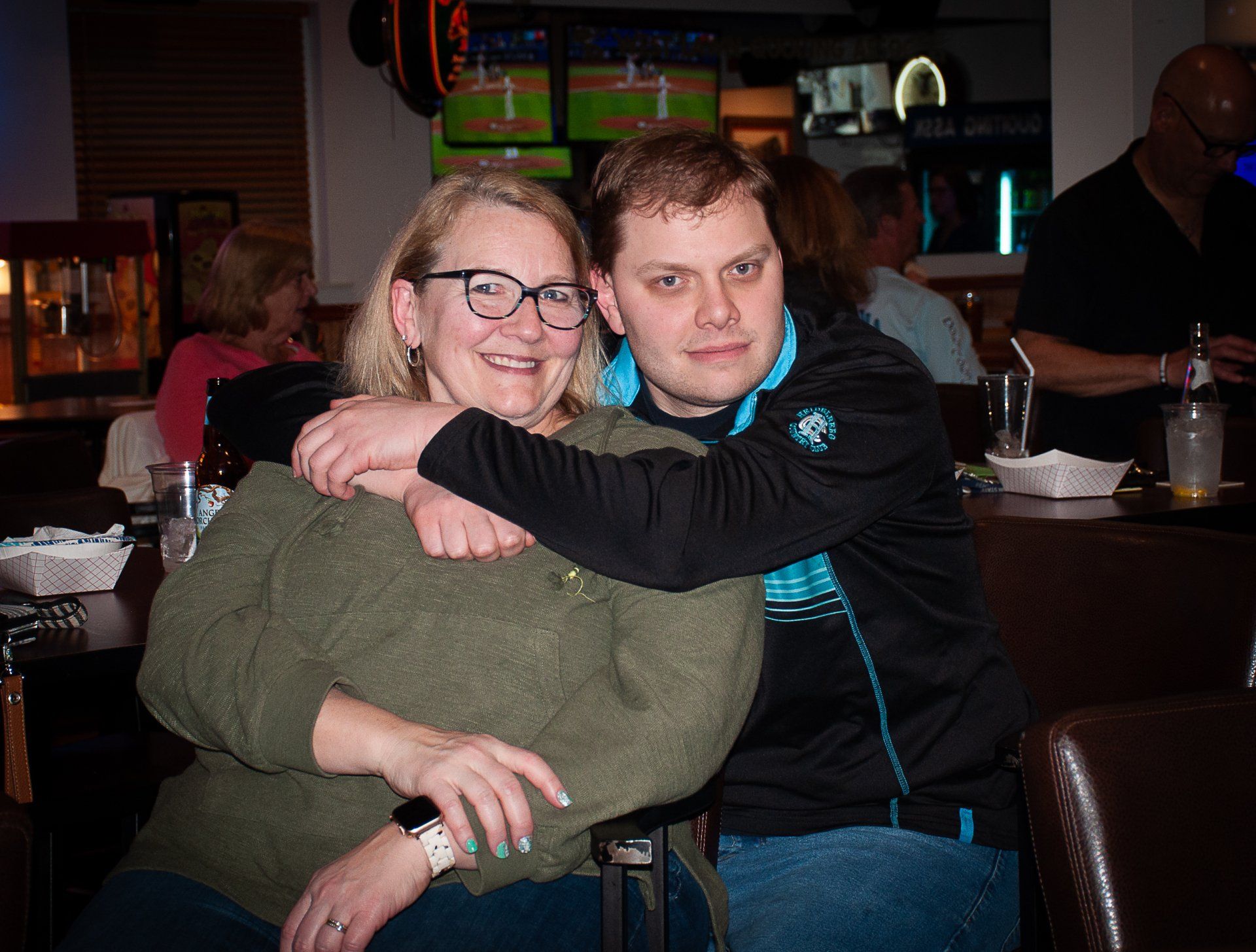 Two people sitting together at a bar, smiling and posing with an arm around each other