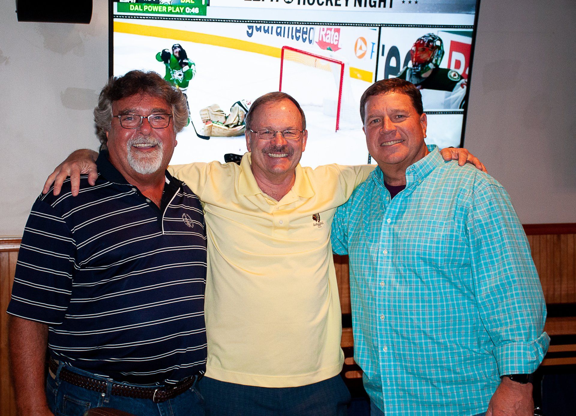 Three smiling people standing together indoors in front of a colorful wall display
