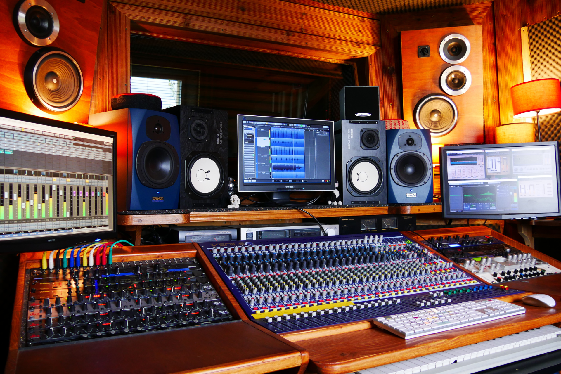 Professional music studio with mixing consoles, speakers, and computer monitors in a warm orange-lit room