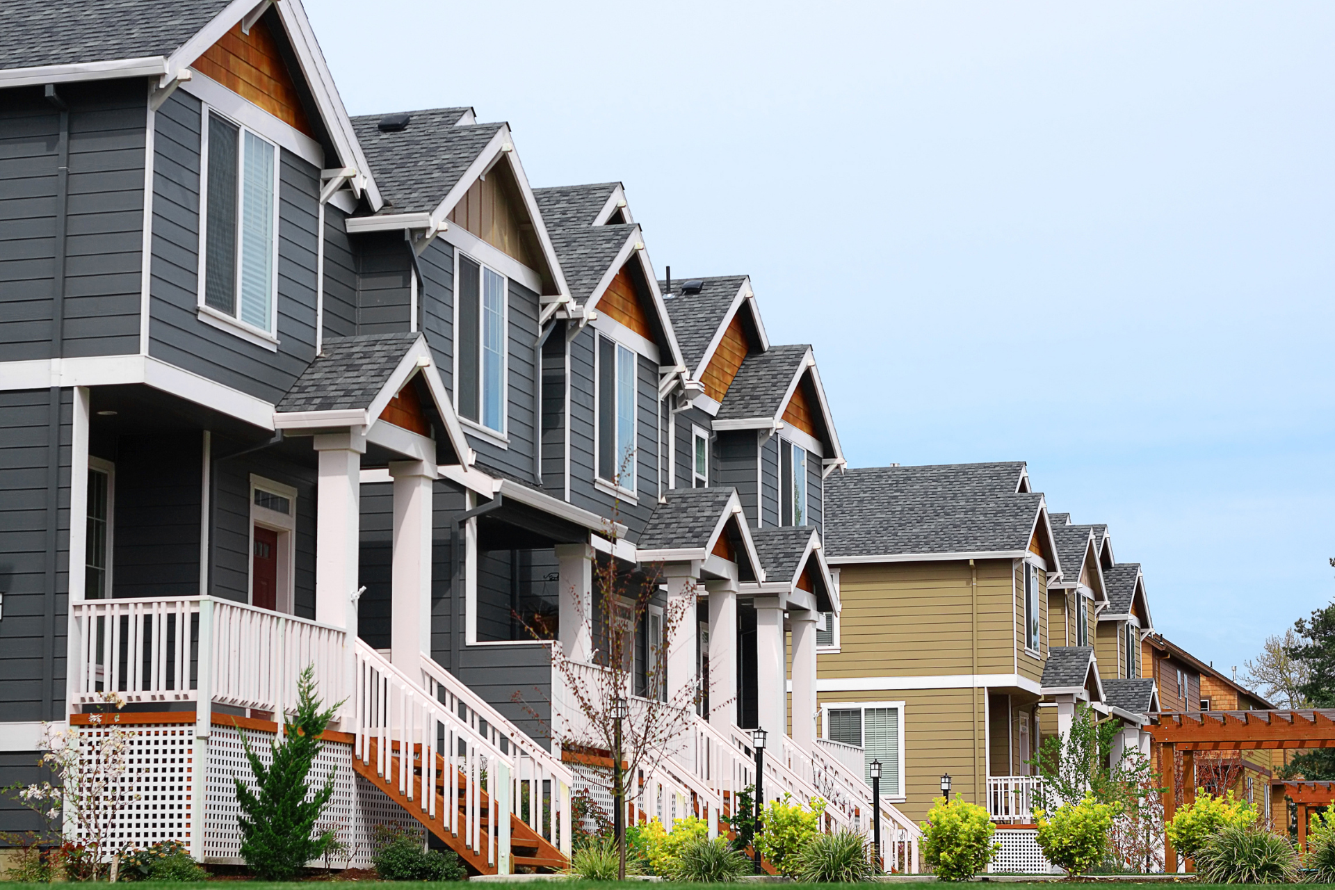 Row of colorful suburban townhouses with porches and peaked roofs under a clear sky