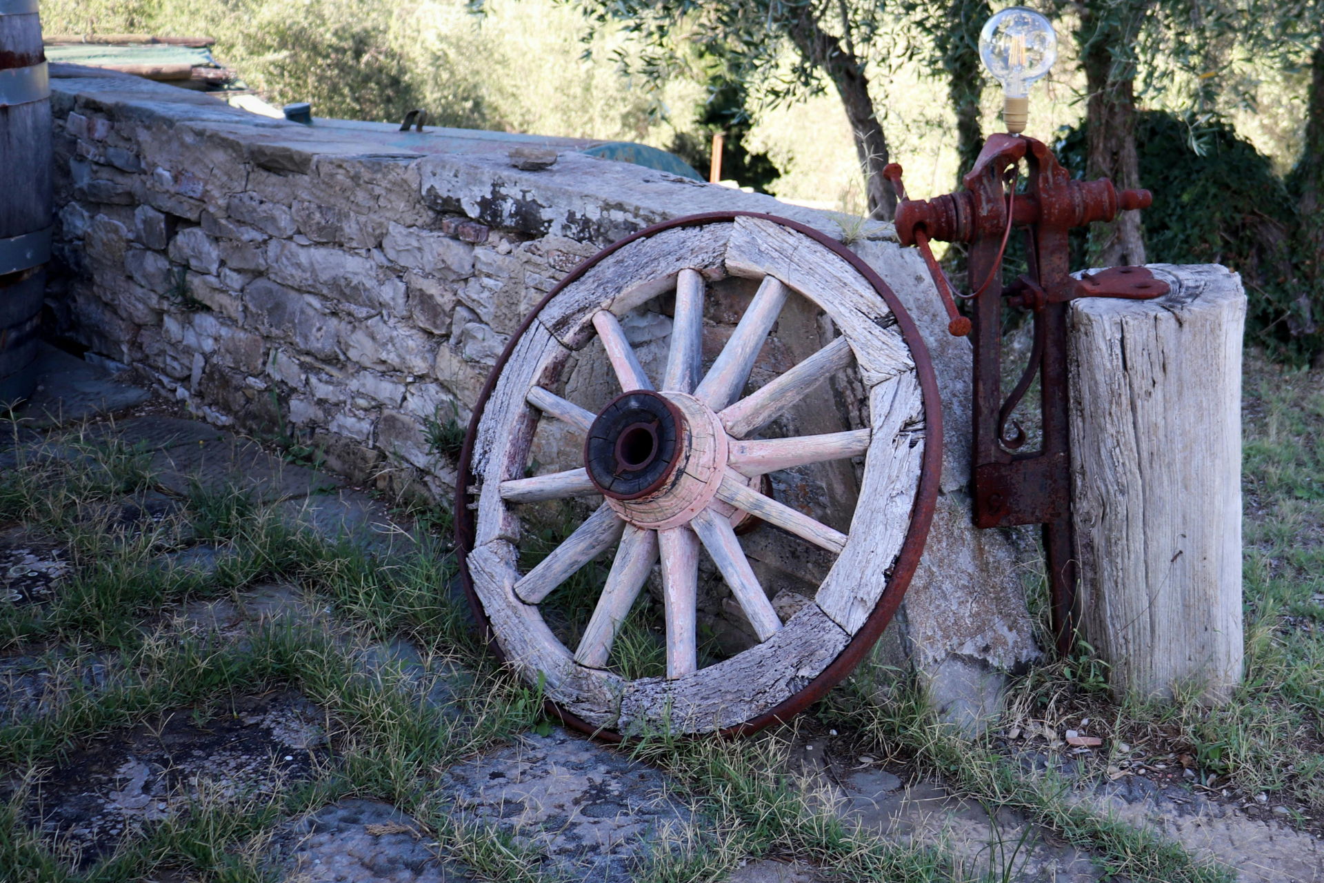 Rustic wooden wagon wheel leaning against a stone wall in a grassy outdoor setting