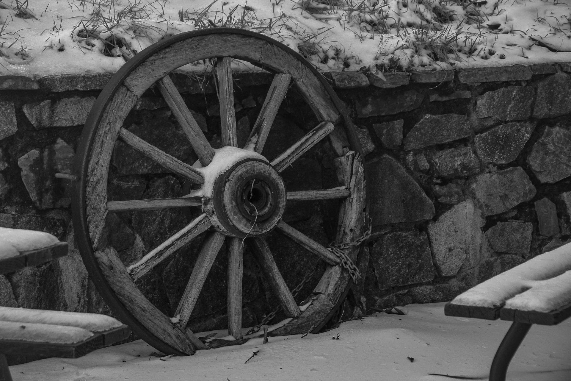Old wooden wagon wheel leaning against a stone wall in a snowy scene.