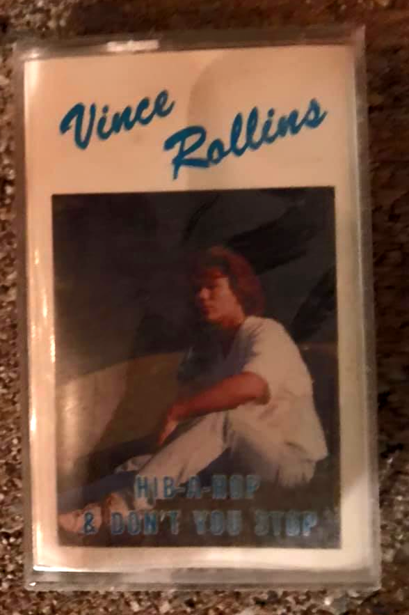 Vince Rollins cassette cover with a seated person on a dark photo background and blue title text