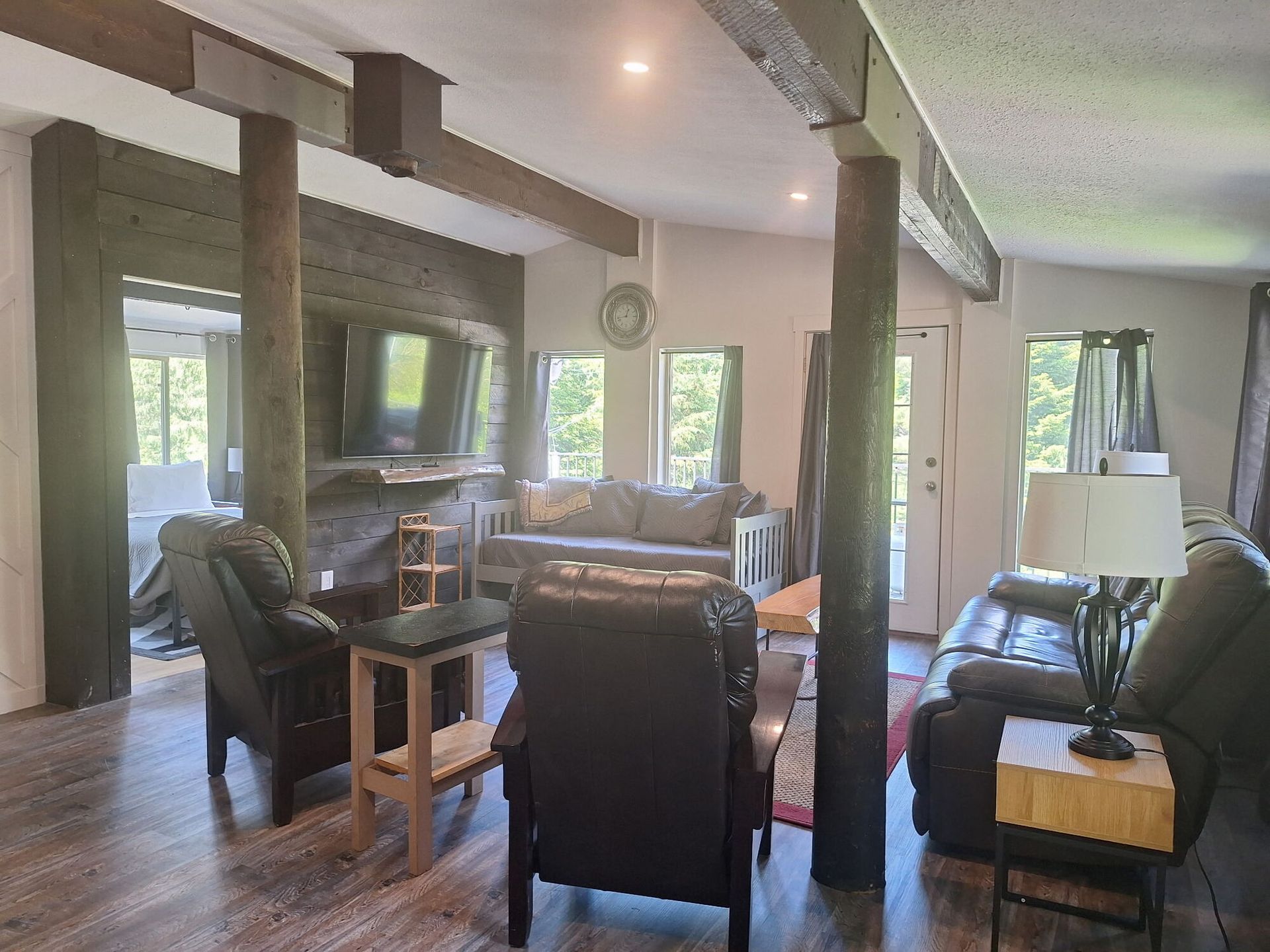Spacious living room with dark leather furniture, large windows, wooden beams, and a dining area in the back