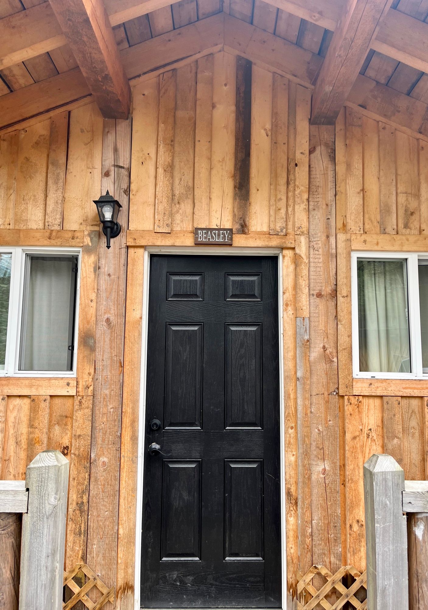 Wooden cabin entrance with black door, lantern, and small windows under a peaked roof