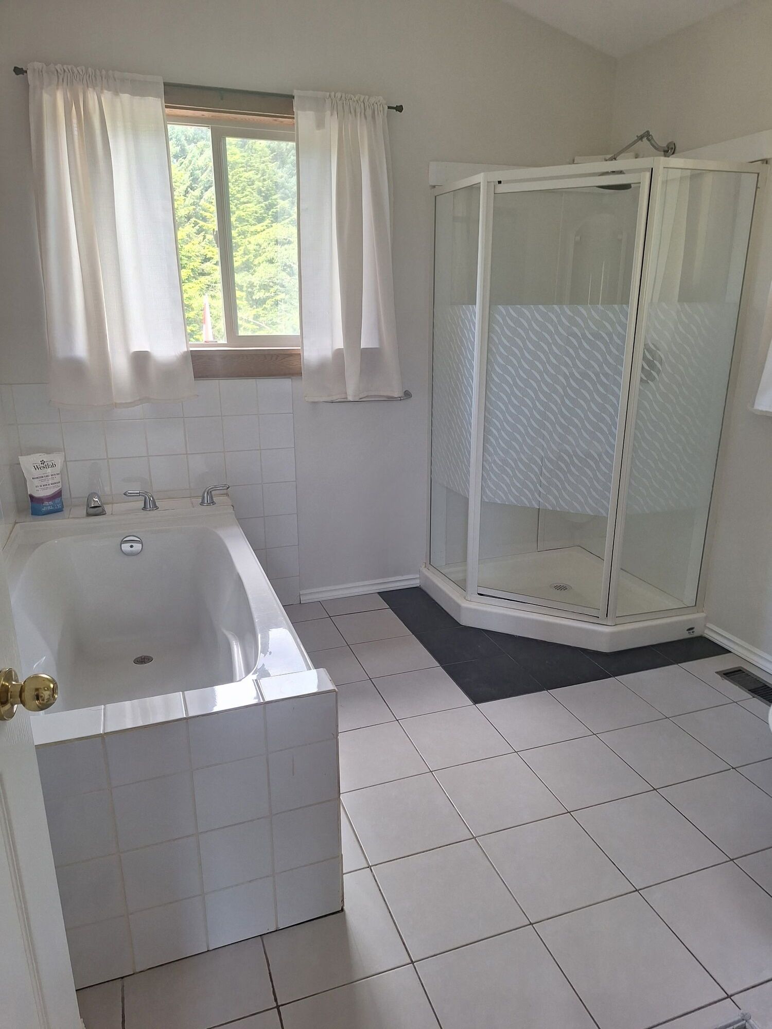 Bright white bathroom with a bathtub, shower stall, and tiled floor near a window.
