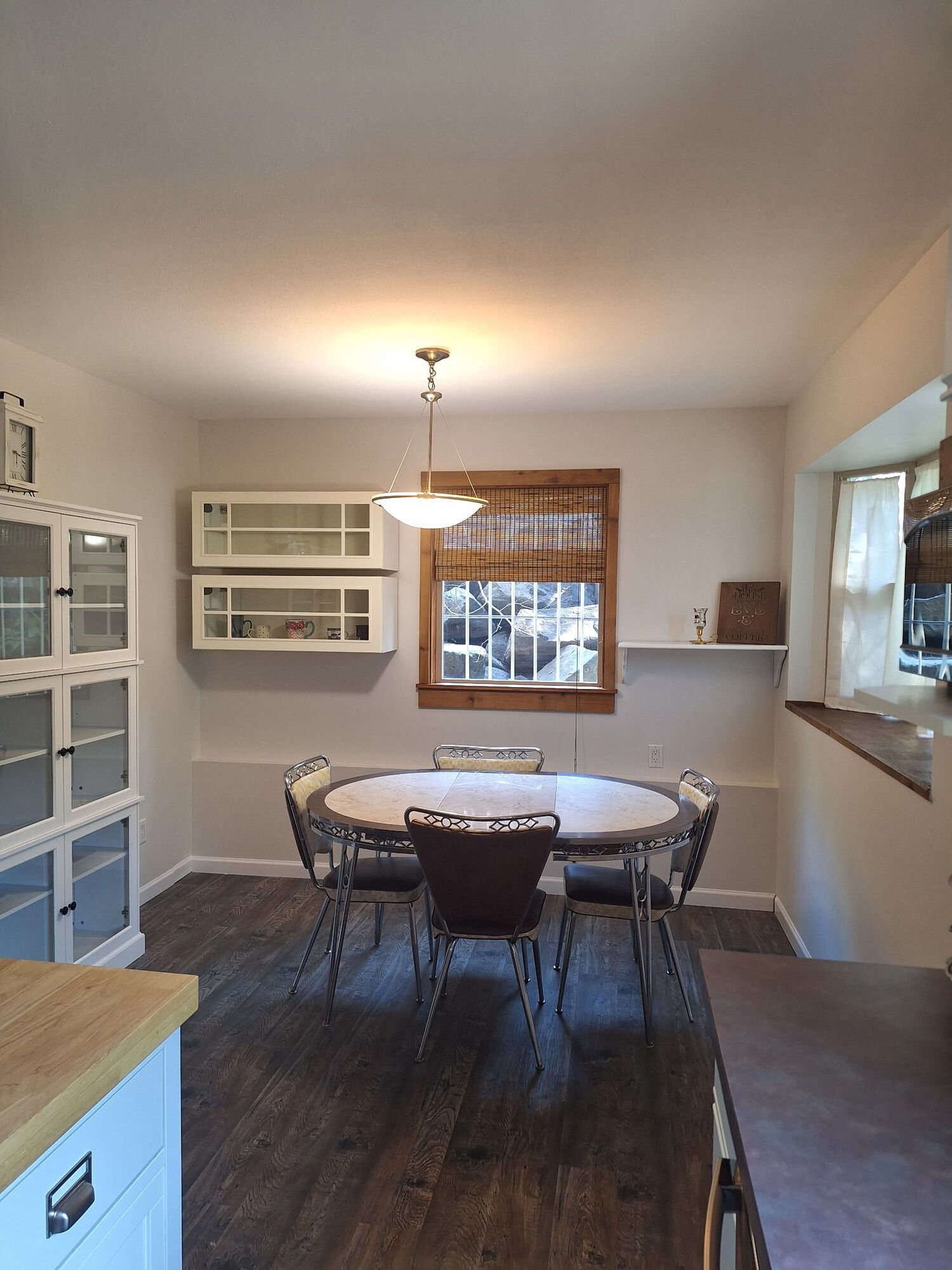 Bright dining room with round table, chairs, dark floor, and cabinets along the walls.