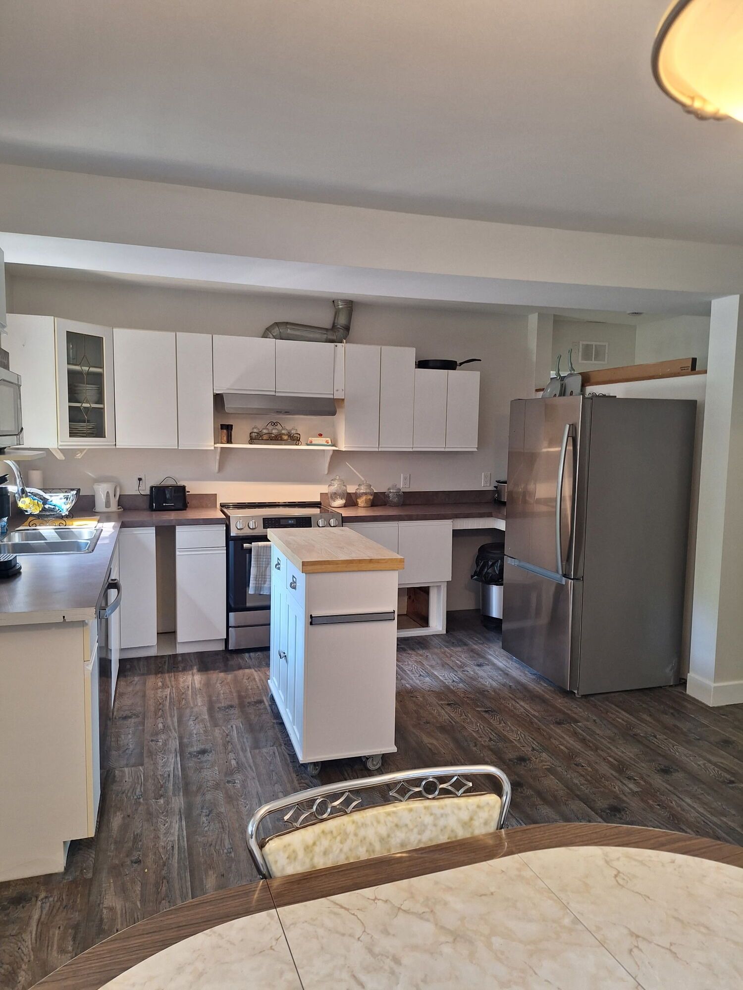 Kitchen and dining area with white cabinets, stainless fridge, island, and wood-look flooring