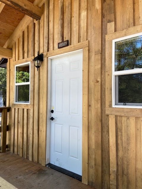 Wooden building exterior with white door and two windows on a covered porch