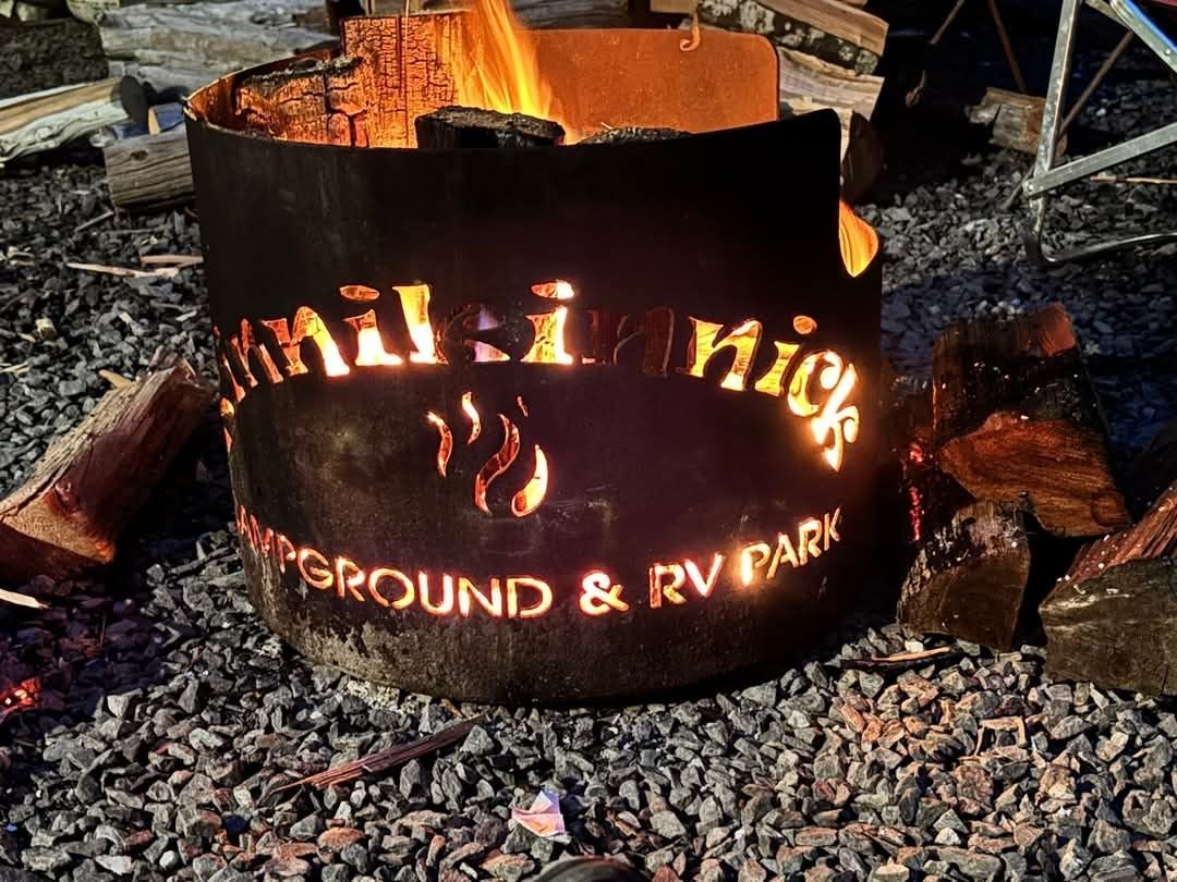 A metal fire pit glowing with flames, with “RV Park” cut out and visible on its side.