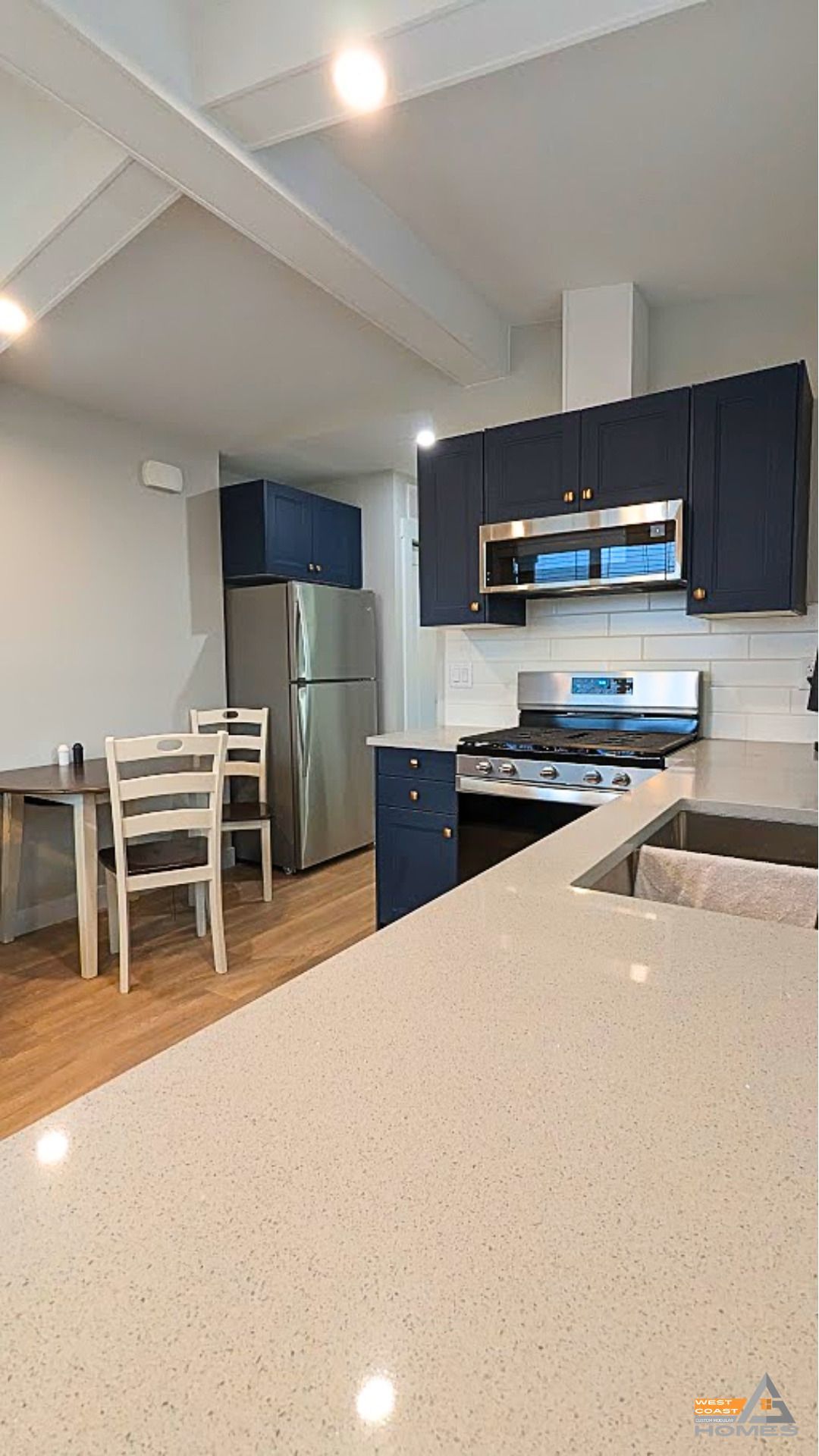 Modern kitchen with dark cabinets, stainless steel appliances, and a light countertop beside a dining area