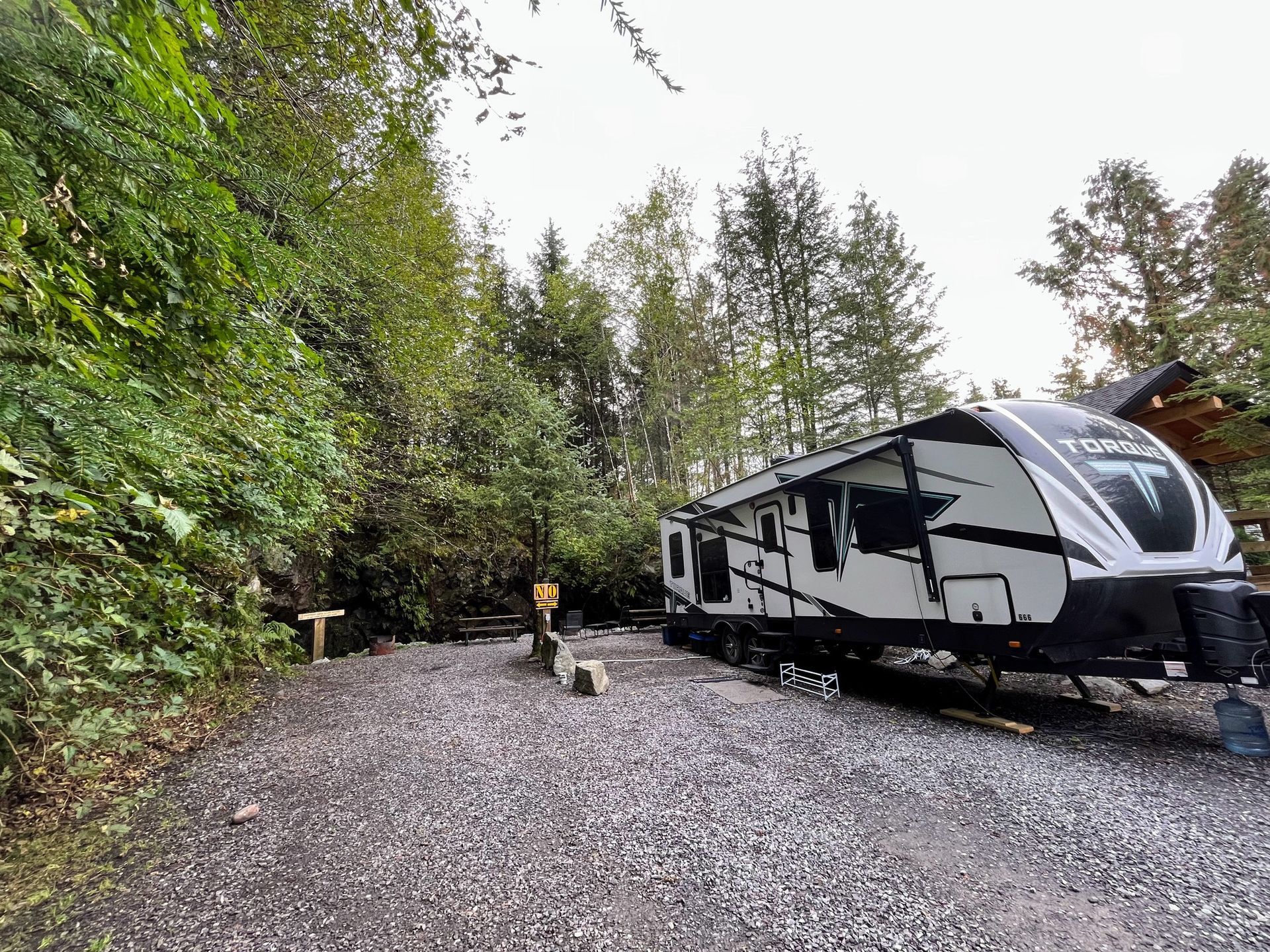 Black and white RV parked on a gravel campsite surrounded by dense green trees