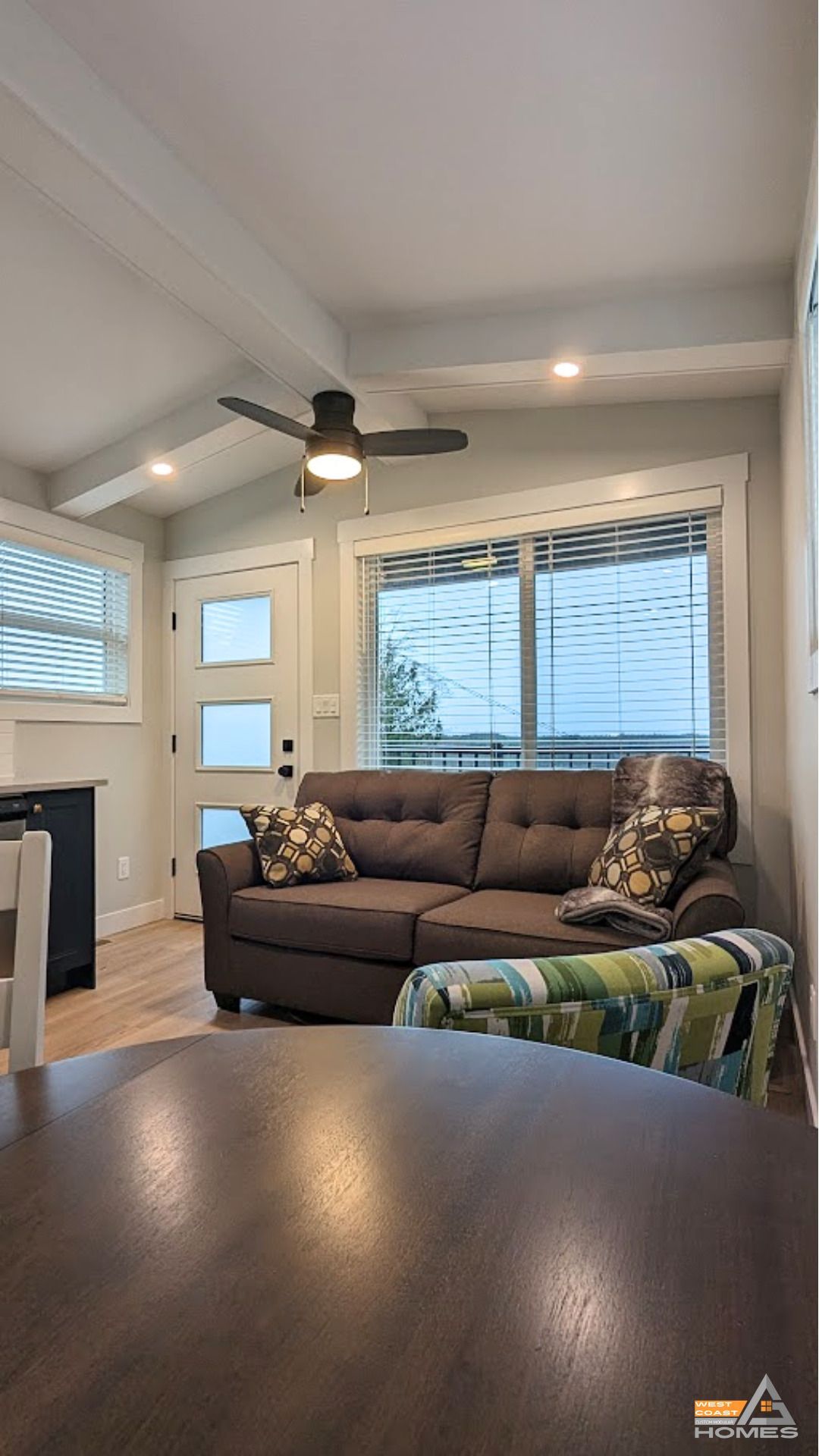 Cozy living room with brown sofa, ceiling fan, large window, and a view of a front door and side windows