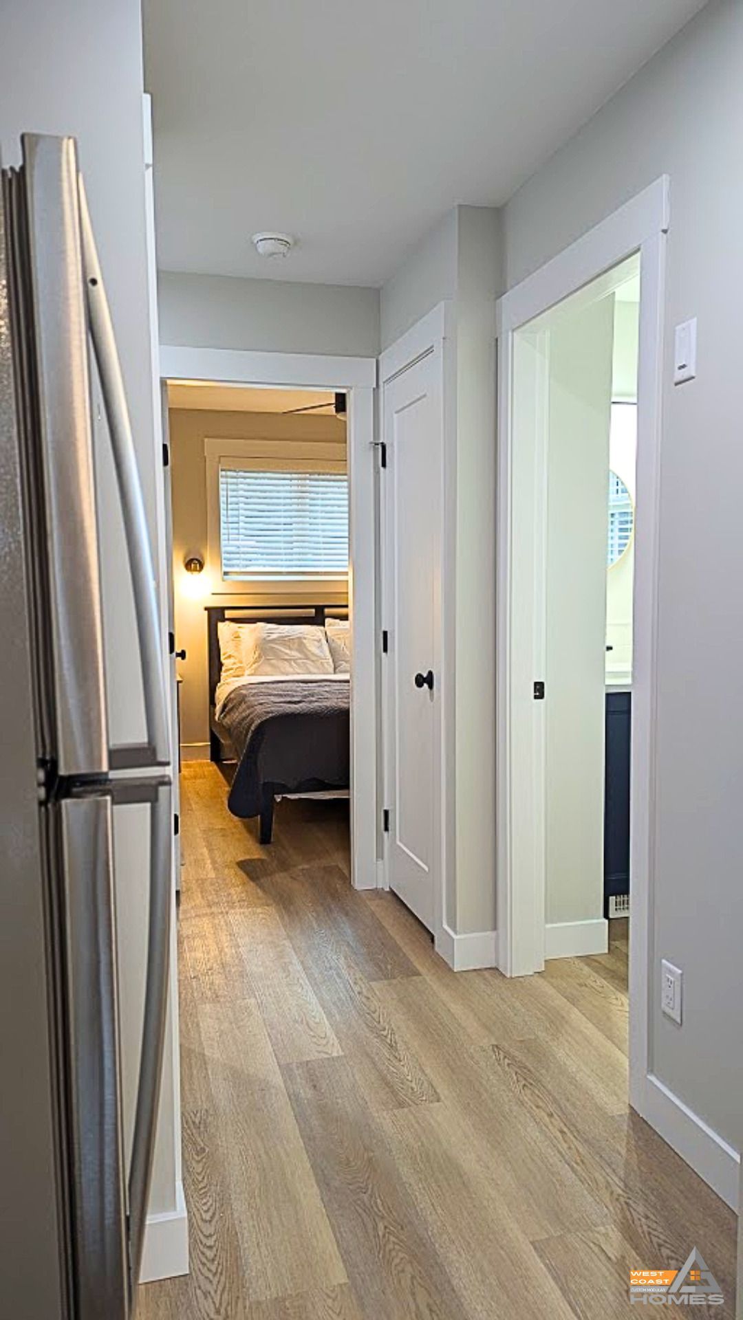 Hallway with light wood floors leading to a bedroom with a made bed and window light