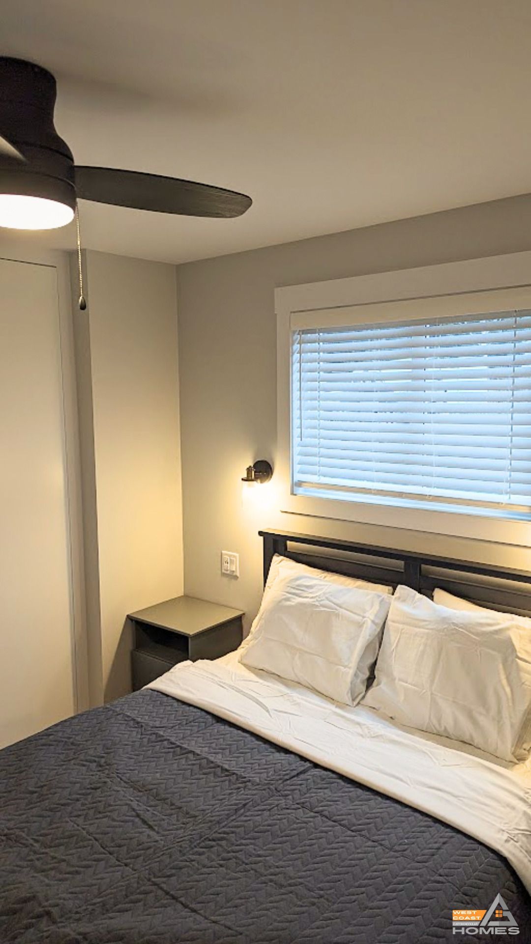 Small bedroom with a bed, gray bedding, white pillows, a ceiling fan, nightstand, and window blinds.